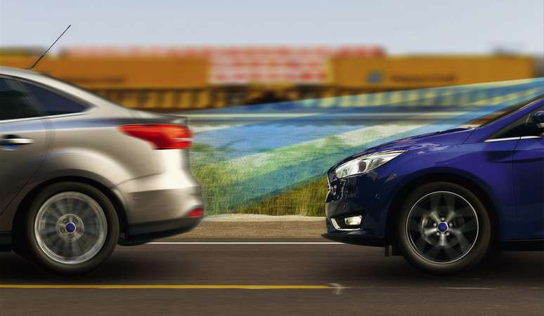 Two cars racing on a highway, one silver and one blue, with a blurred background of greenery and a train.