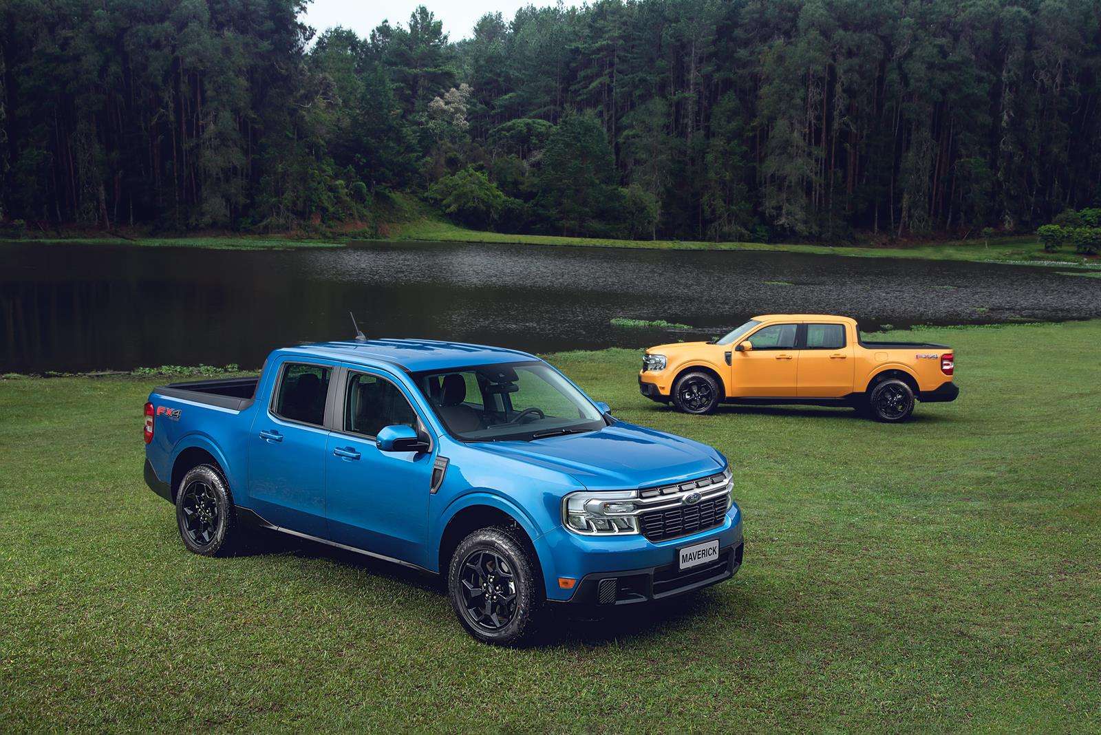 A blue pickup truck parked on green grass near a lake, with a yellow pickup truck visible in the background.