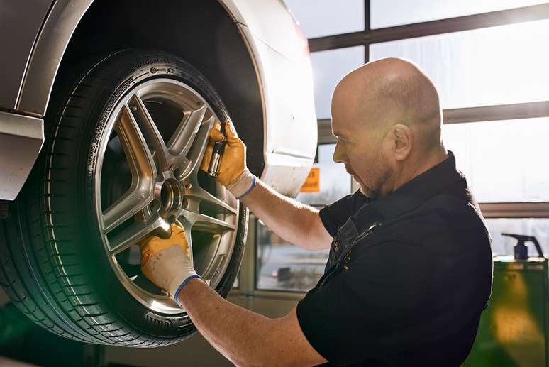 A mechanic inspecting a car wheel while using a tool in a well-lit garage.