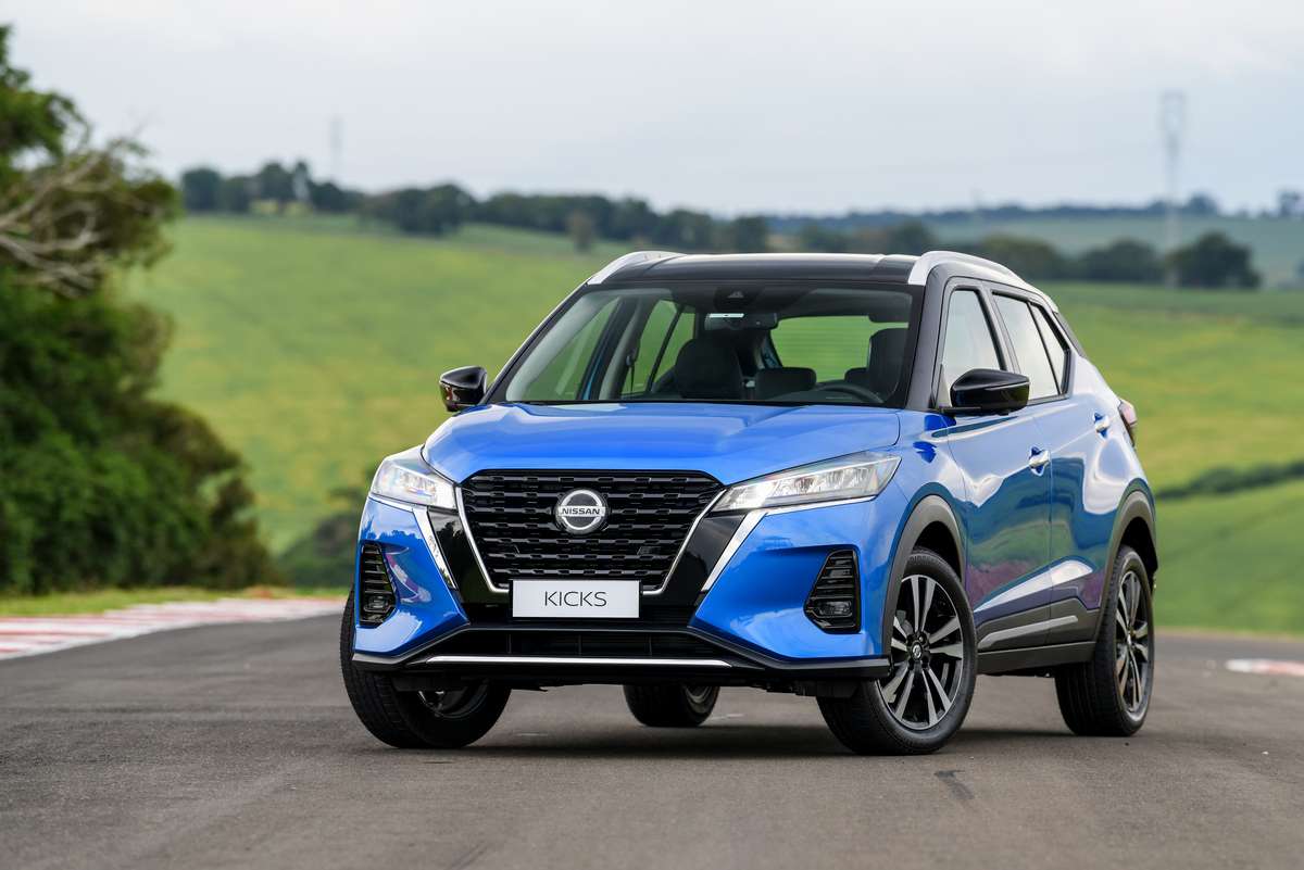 A blue Nissan Kicks SUV parked on a scenic road with green hills in the background.