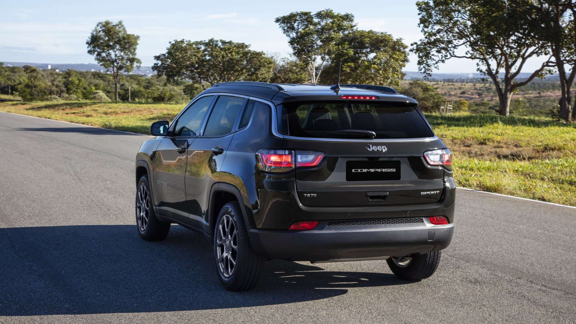 Um SUV Jeep Compass preto visto de trás, em uma estrada cercada por árvores e vegetação.