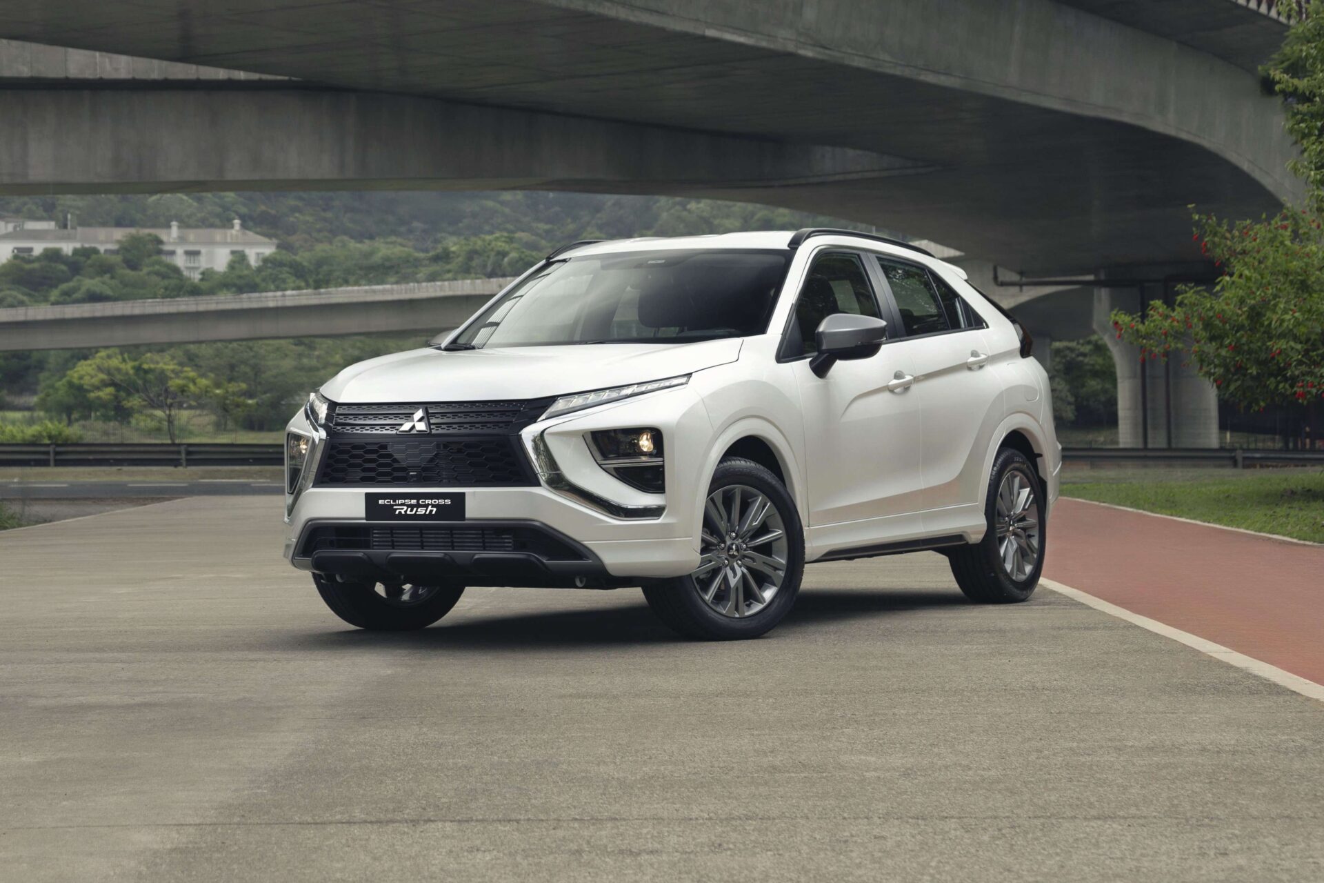 A white Mitsubishi Eclipse Cross parked on a smooth road with concrete overpasses in the background.