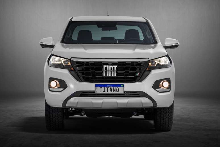 Front view of a white Fiat pickup truck with a prominent grille, illuminated headlights, and a license plate reading 'TITANO'.