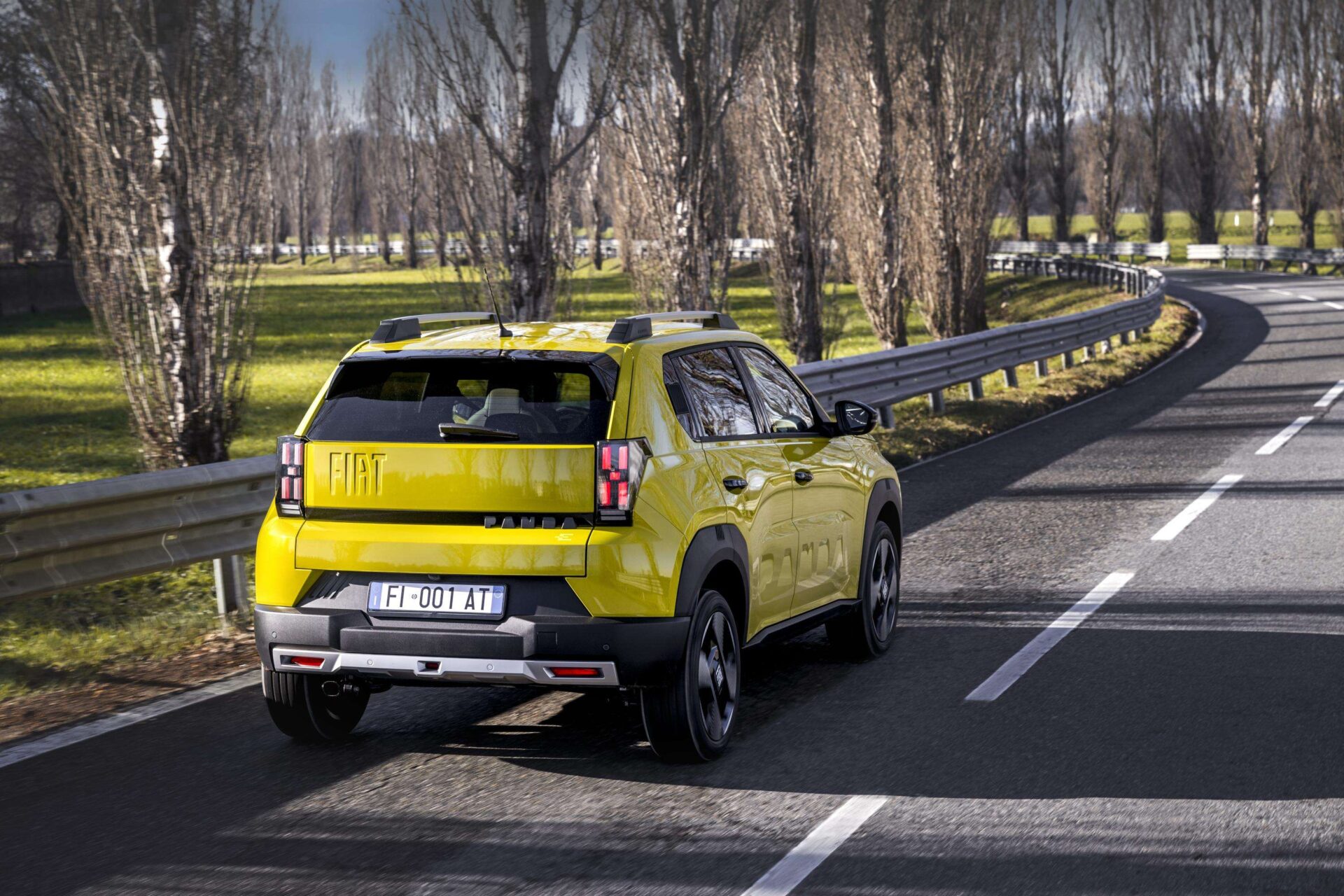 A vibrant yellow SUV driving along a curved road surrounded by trees and green fields.