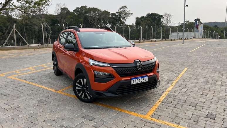 A vibrant orange Renault SUV parked in an empty lot, surrounded by greenery and a fence.