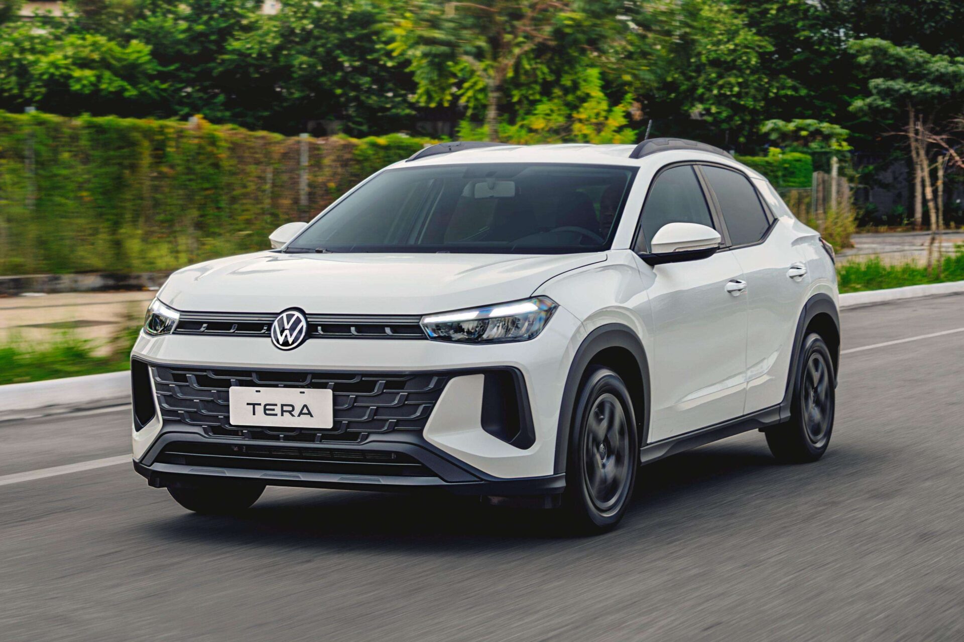 Carro SUV branco da Volkswagen, modelo TERA, em movimento em uma estrada com vegetação ao fundo.
