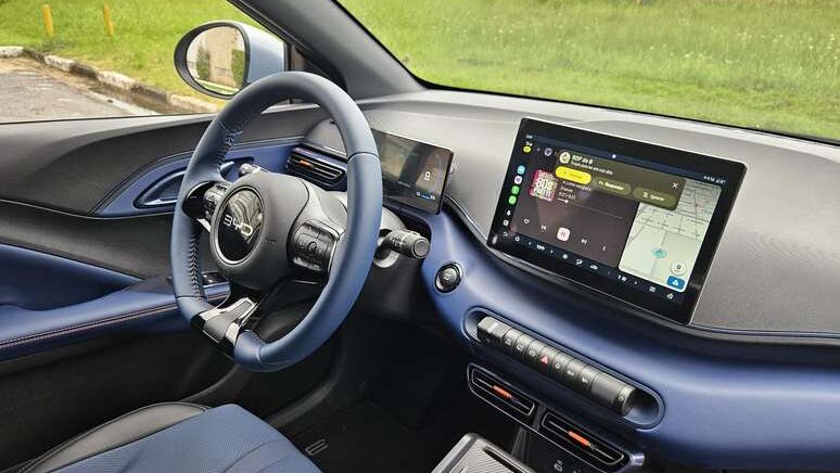 Interior de um carro mostrando o volante e a tela do painel, com foco em tecnologia e design modernista.