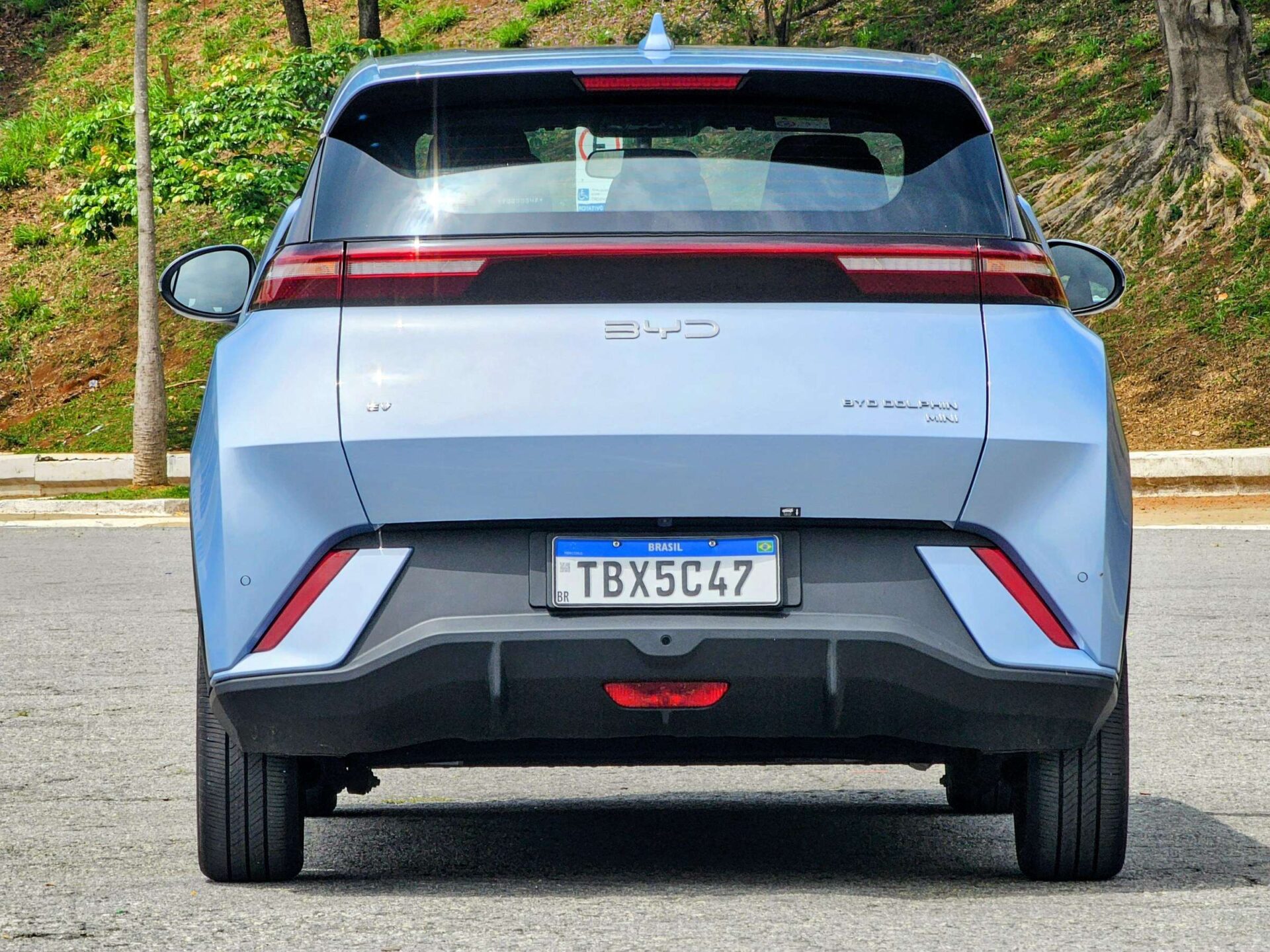 Visão traseira de um carro elétrico azul BYD Dolphin Mini estacionado em uma área ao ar livre.