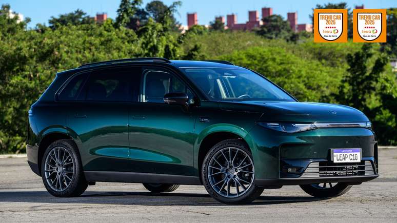 Side view of a green electric SUV parked outdoors with a blurred background of trees and buildings. The vehicle features modern design elements and alloy wheels. Awards are displayed in the corner indicating 'Trend Car 2025'.