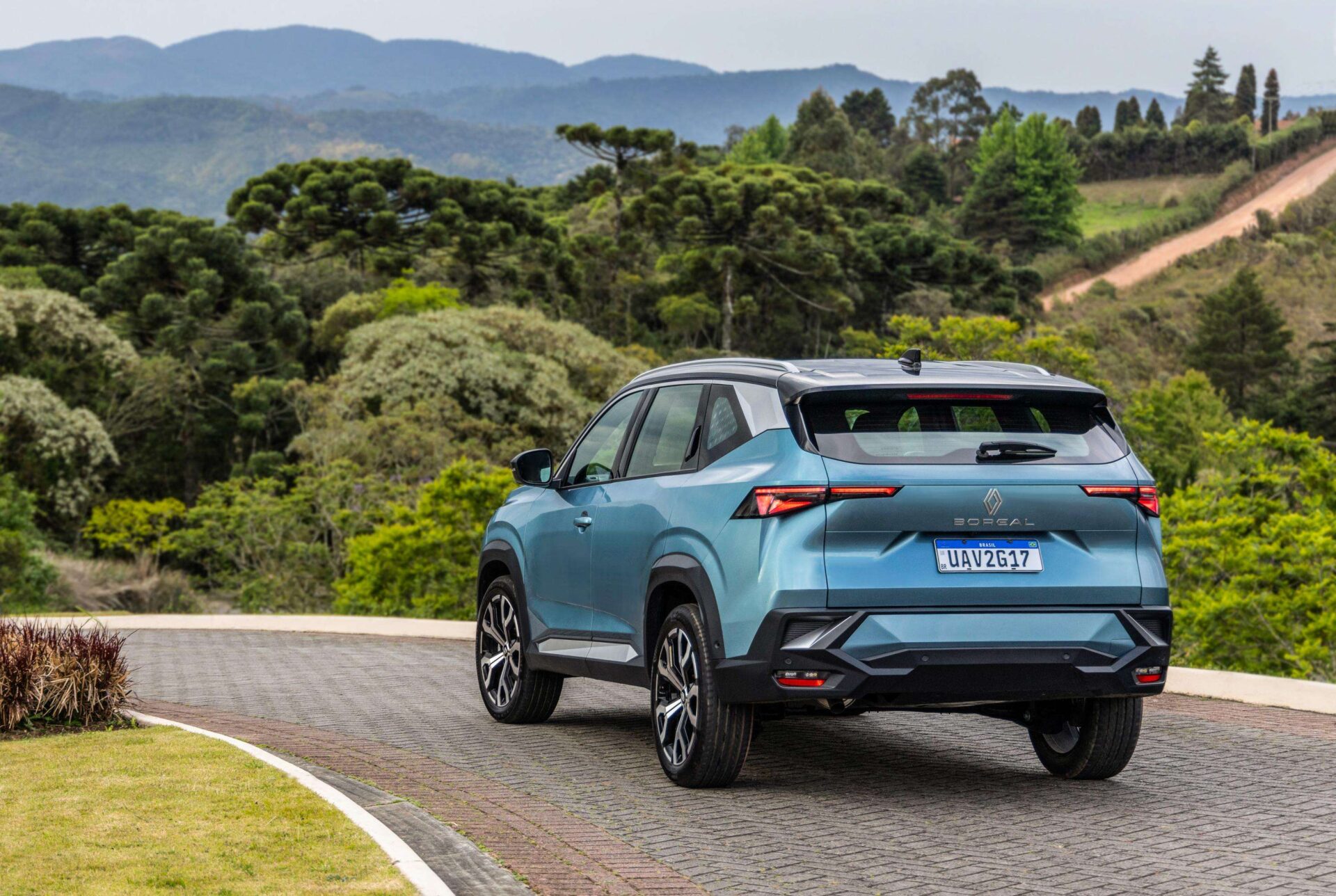 A blue SUV parked on a winding road surrounded by lush green trees and distant mountains.