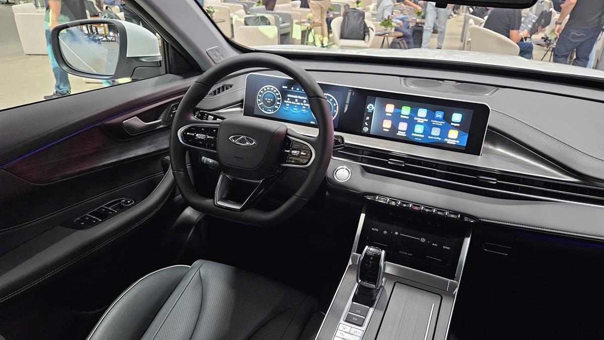 Interior de um carro com volante moderno, painel digital e tela central de entretenimento com aplicativos.