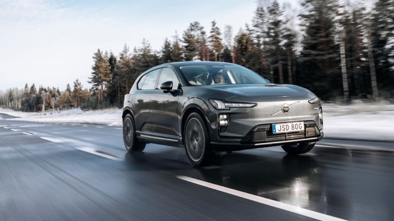 A modern electric car speeding along a wet road, surrounded by snow-covered trees.