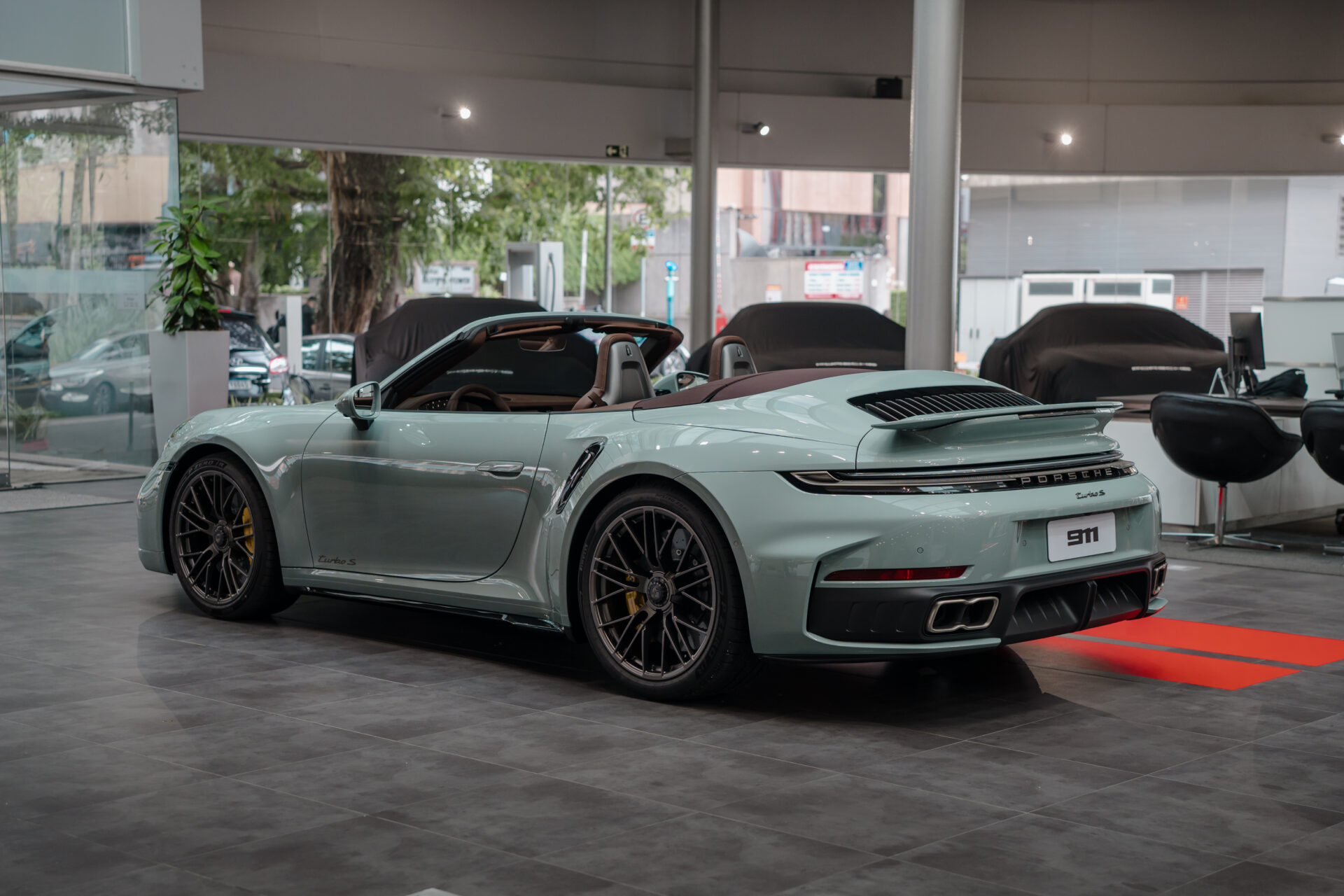 A mint green Porsche 911 Turbo S convertible parked in a modern car showroom, showcasing its sleek design and stylish features.