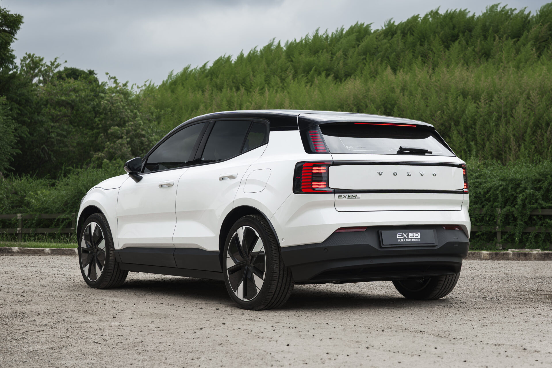 A white Volvo EX30 parked on a gravel surface with greenery in the background.