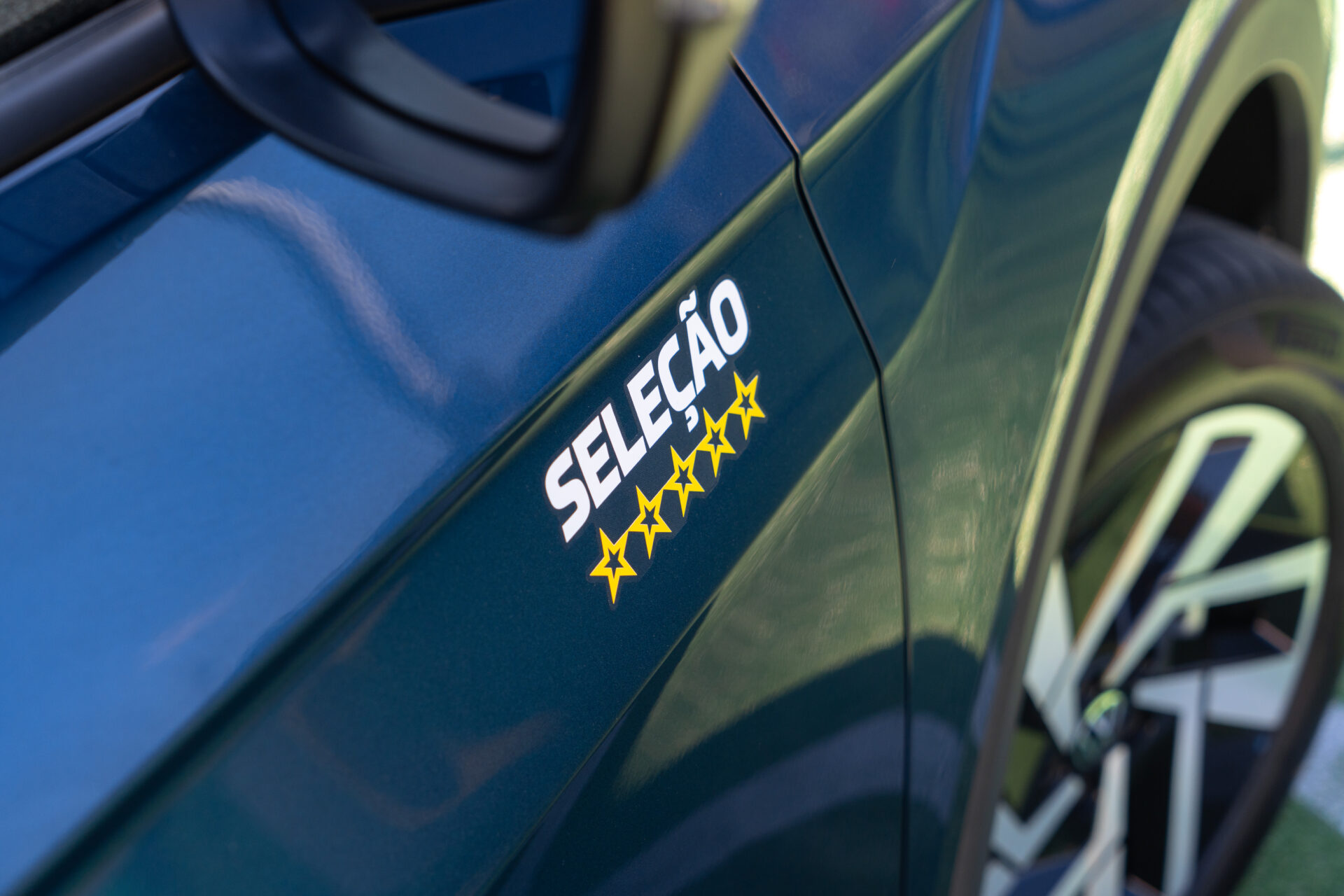 Detalhe da lateral de um carro azul com a inscrição 'SELEÇÃO' e cinco estrelas amarelas ao lado.