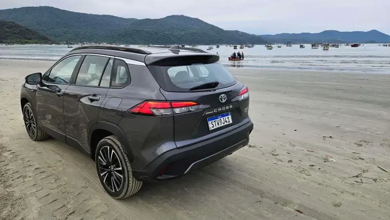 A gray Toyota SUV parked on a sandy beach with mountains and boats in the background.