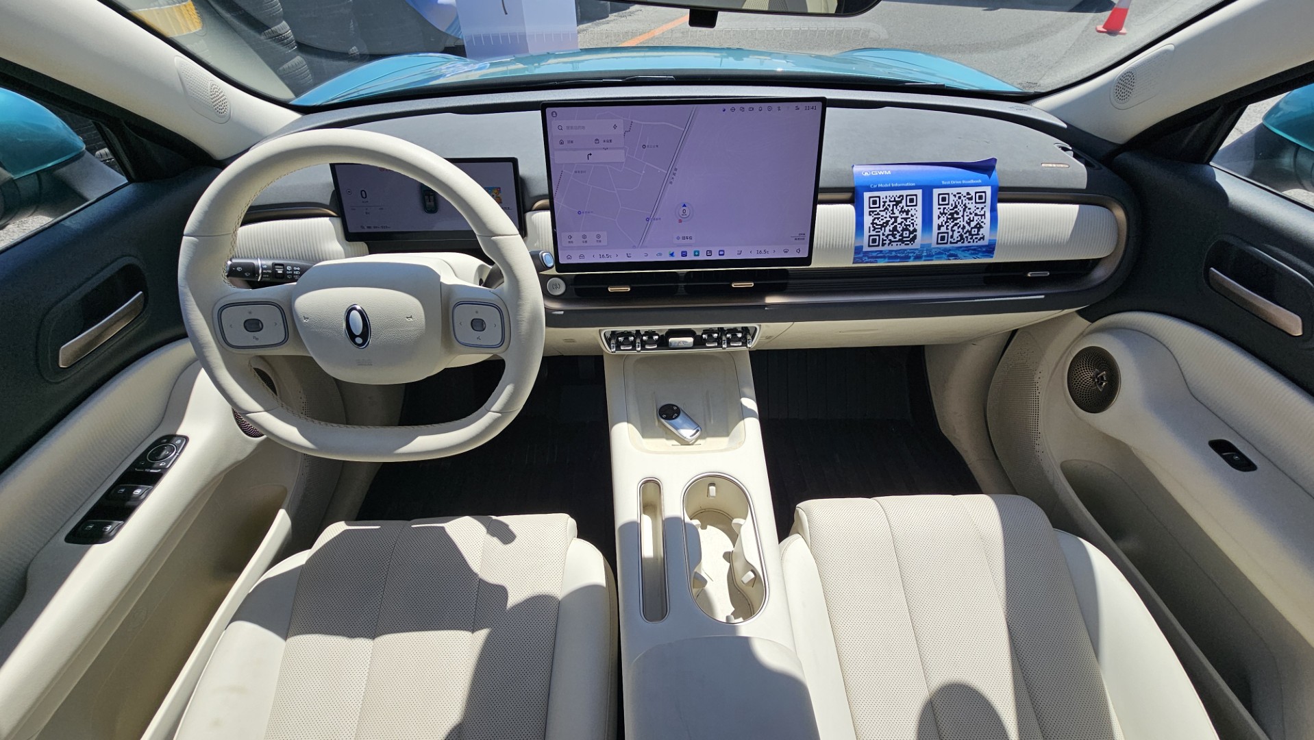 Interior view of a modern car dashboard featuring a large central touchscreen display, a steering wheel with control buttons, and various console controls and storage compartments.
