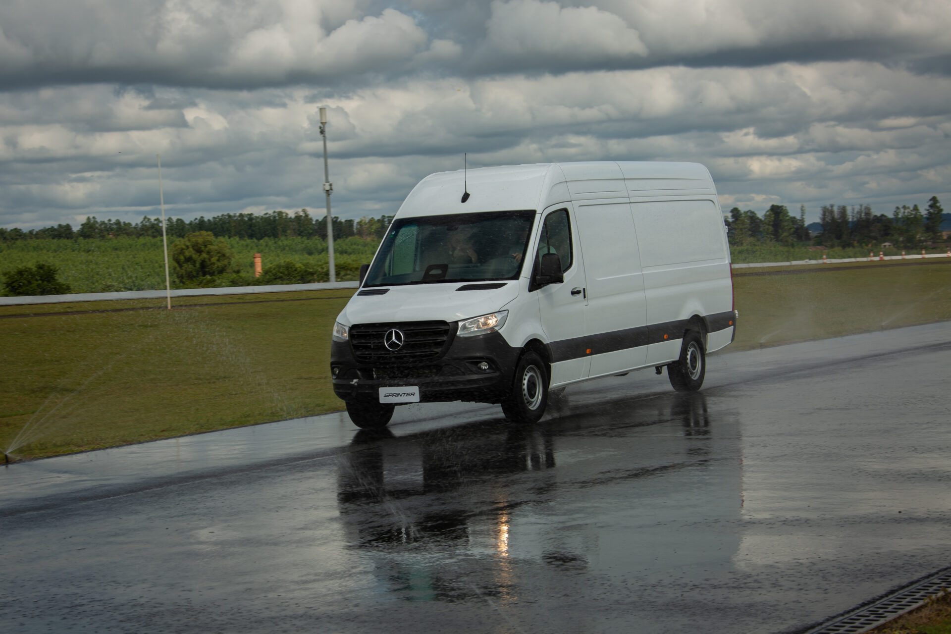Furgão Mercedes-Benz Sprinter em uma pista molhada, com céu nublado ao fundo.