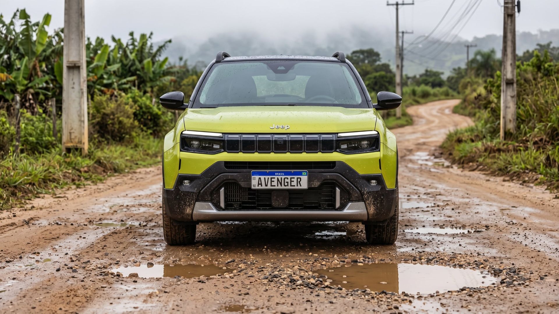 Front view of a green Jeep Avenger parked on a muddy dirt road surrounded by lush vegetation.