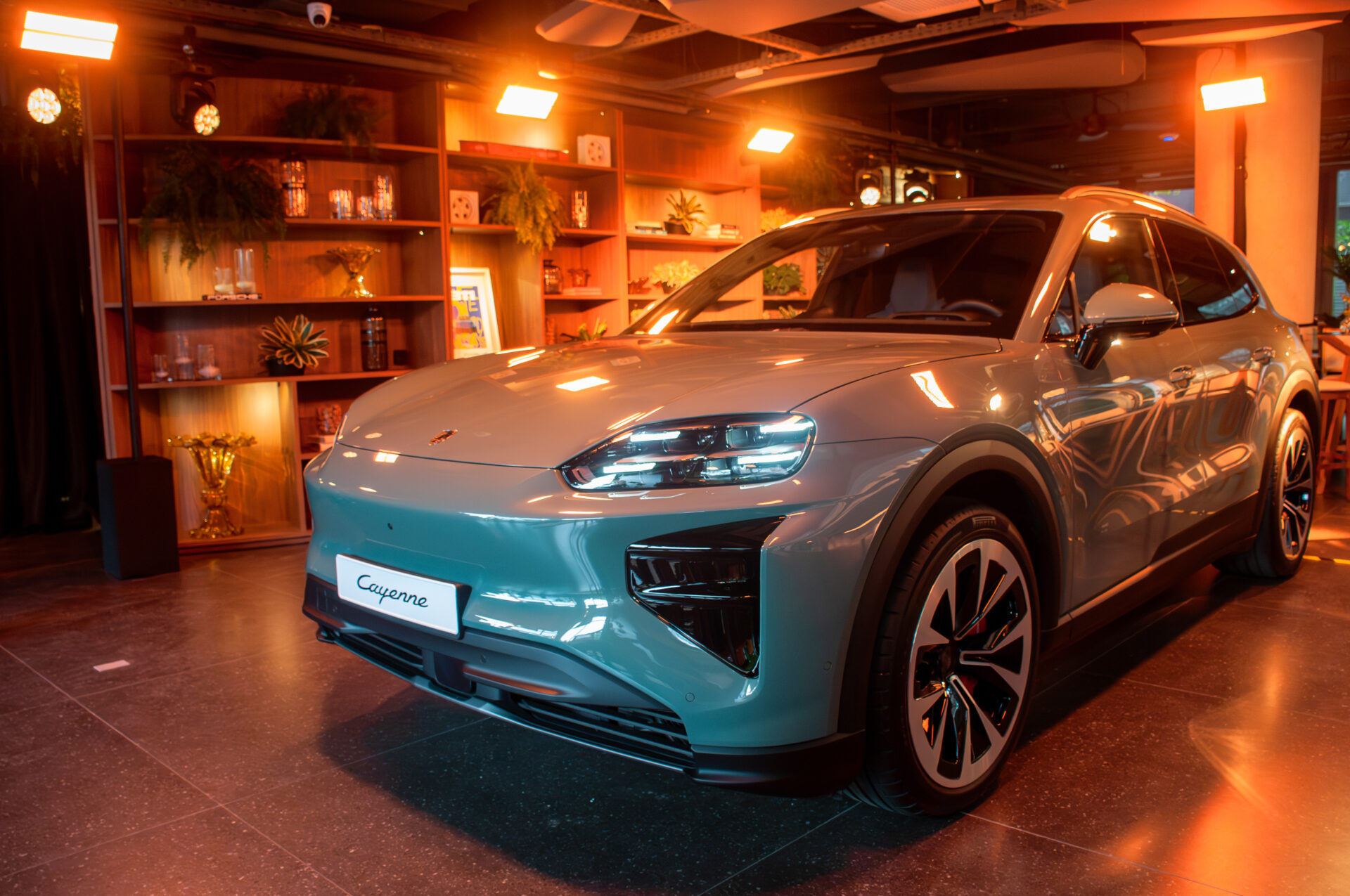 SUV Porsche Cayenne em ambiente interno, com iluminação suave, destacando a carroceria em tom azul claro e detalhes elegantes.