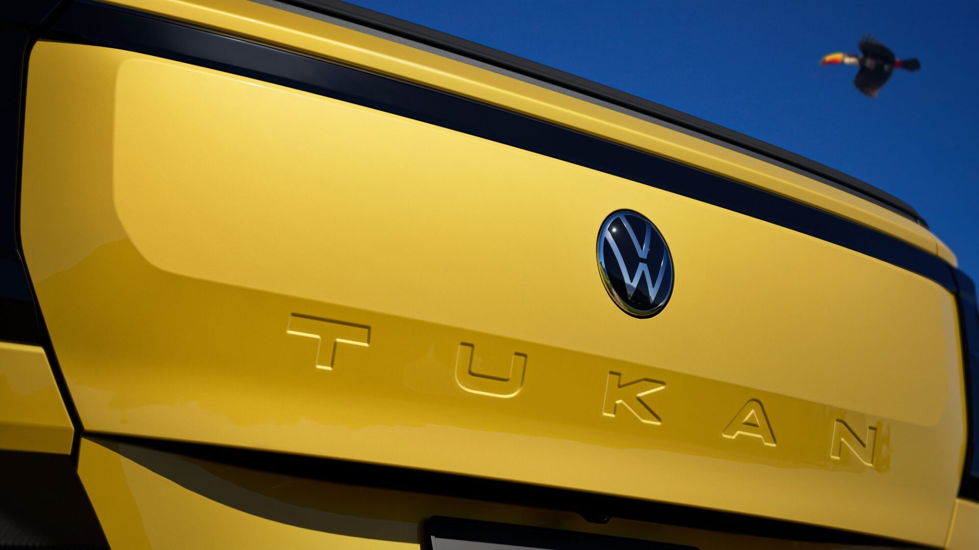 Close-up of the rear of a Volkswagen vehicle featuring a bright yellow finish, the Volkswagen logo, and the model name 'TUKAN' embossed in the body.