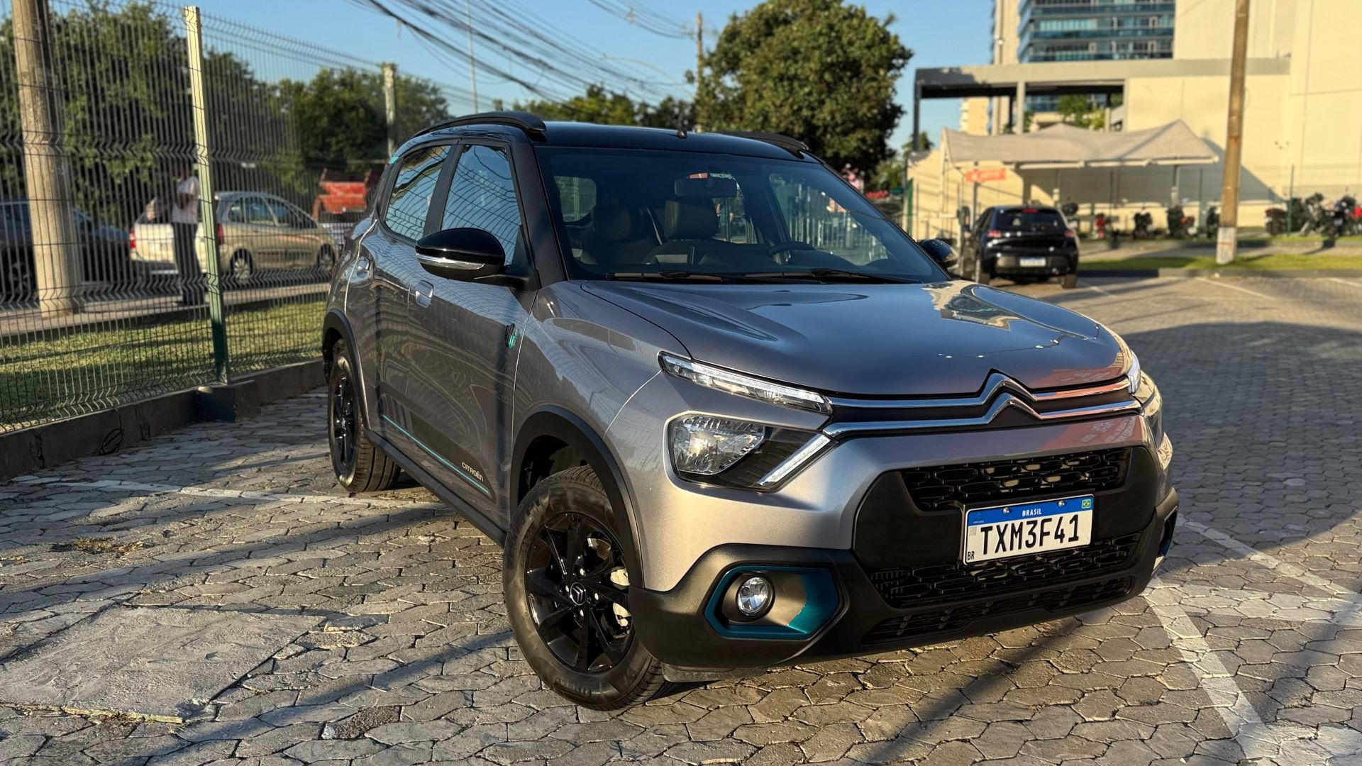 A silver compact SUV parked on a cobblestone surface with a fence and trees in the background.