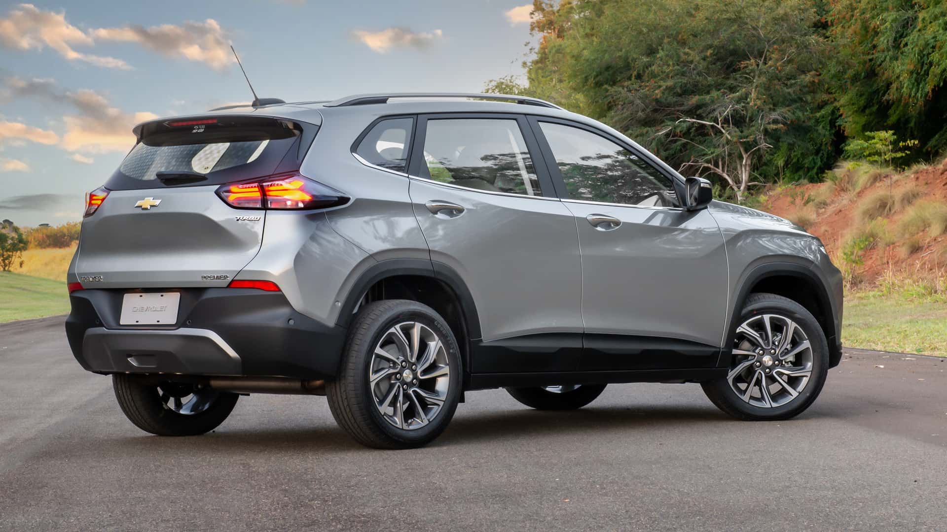 SUV Chevrolet Tracker na cor prata, vista lateral traseira, estacionado em uma estrada com vegetação ao fundo.