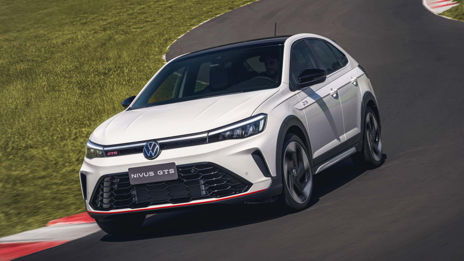 A white Volkswagen Nivus GTS sports car driving on a racetrack, showcasing its sleek design and aggressive stance.