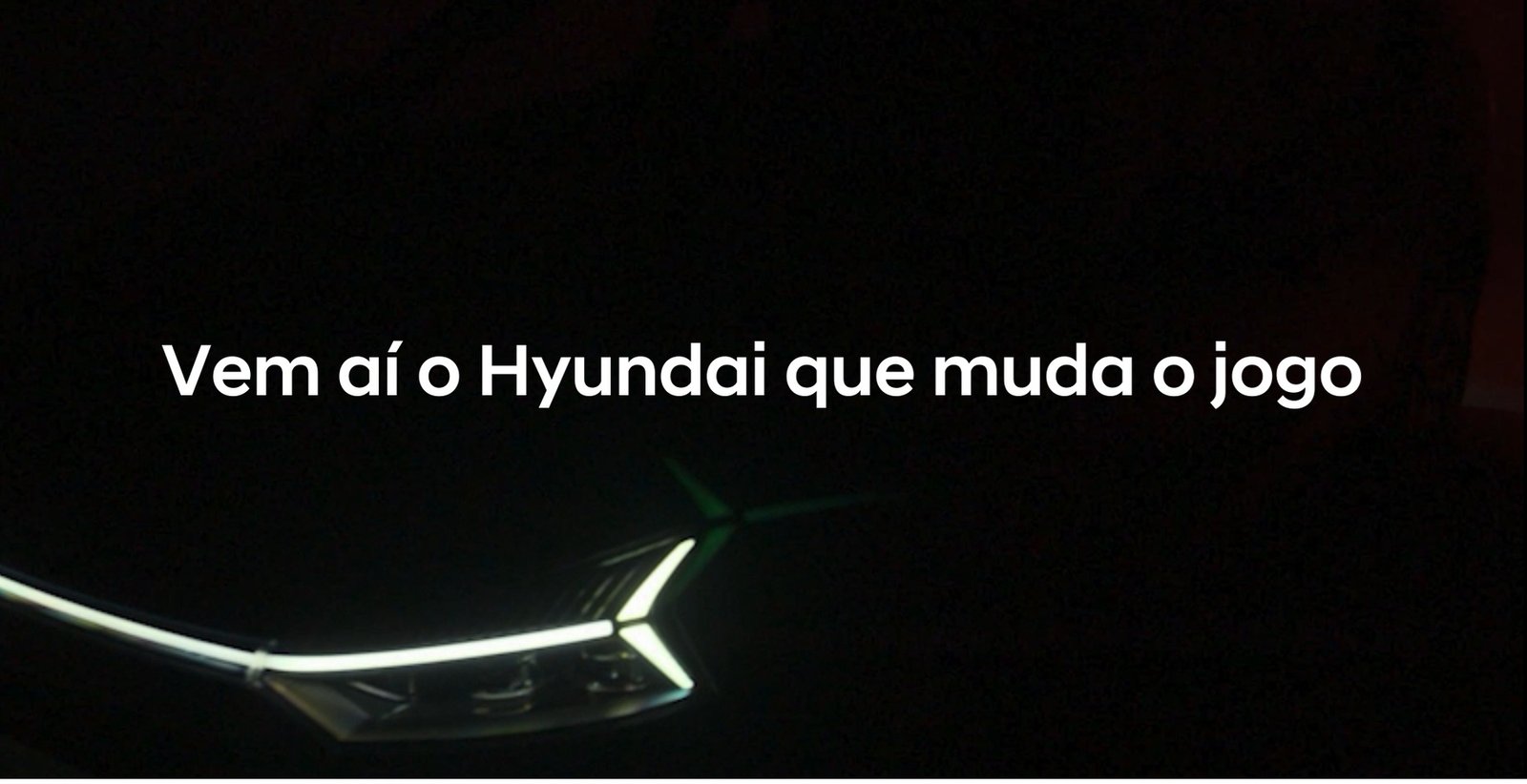 A dark image featuring the tagline 'Vem aí o Hyundai que muda o jogo' with a partially illuminated car headlight in the foreground.