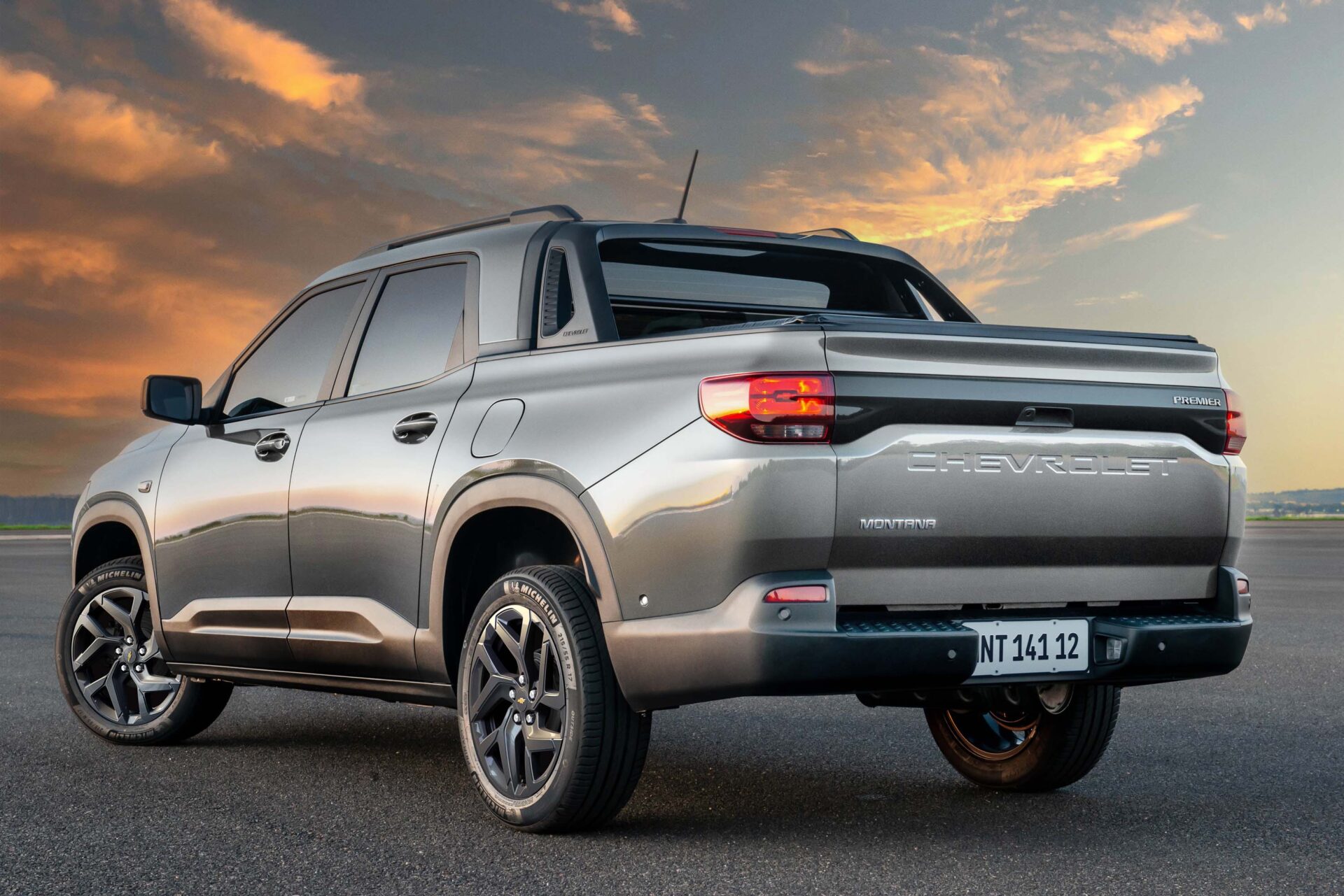 A silver Chevrolet Montana pickup truck parked on a smooth road with a dramatic sunset sky in the background.