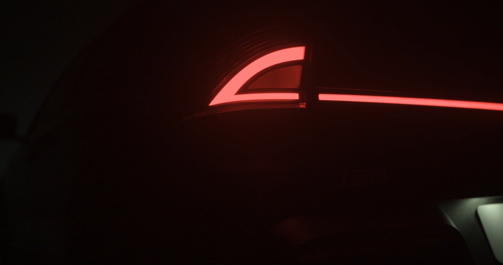 Close-up of a car's rear light featuring a glowing red design against a dark background.