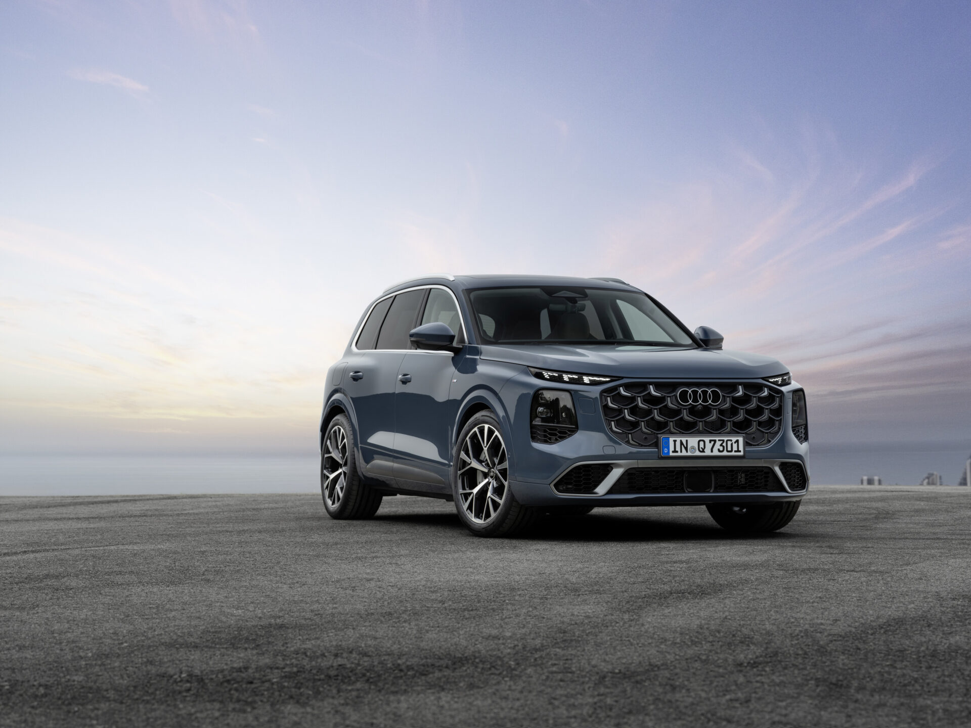 A modern blue Audi SUV parked on a smooth surface during sunset, showcasing its sleek design and distinctive grille.