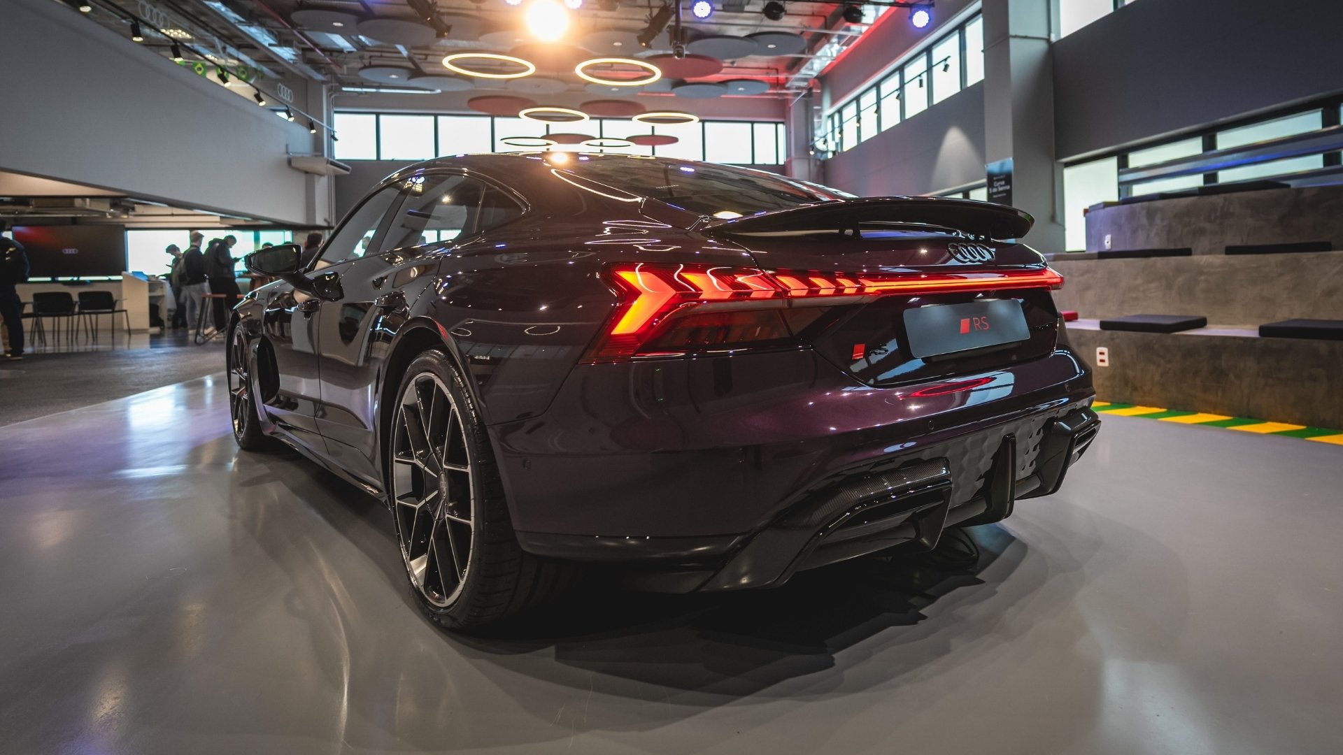 Rear view of a sleek purple Audi RS car in a modern showroom setting with bright lights and large windows.