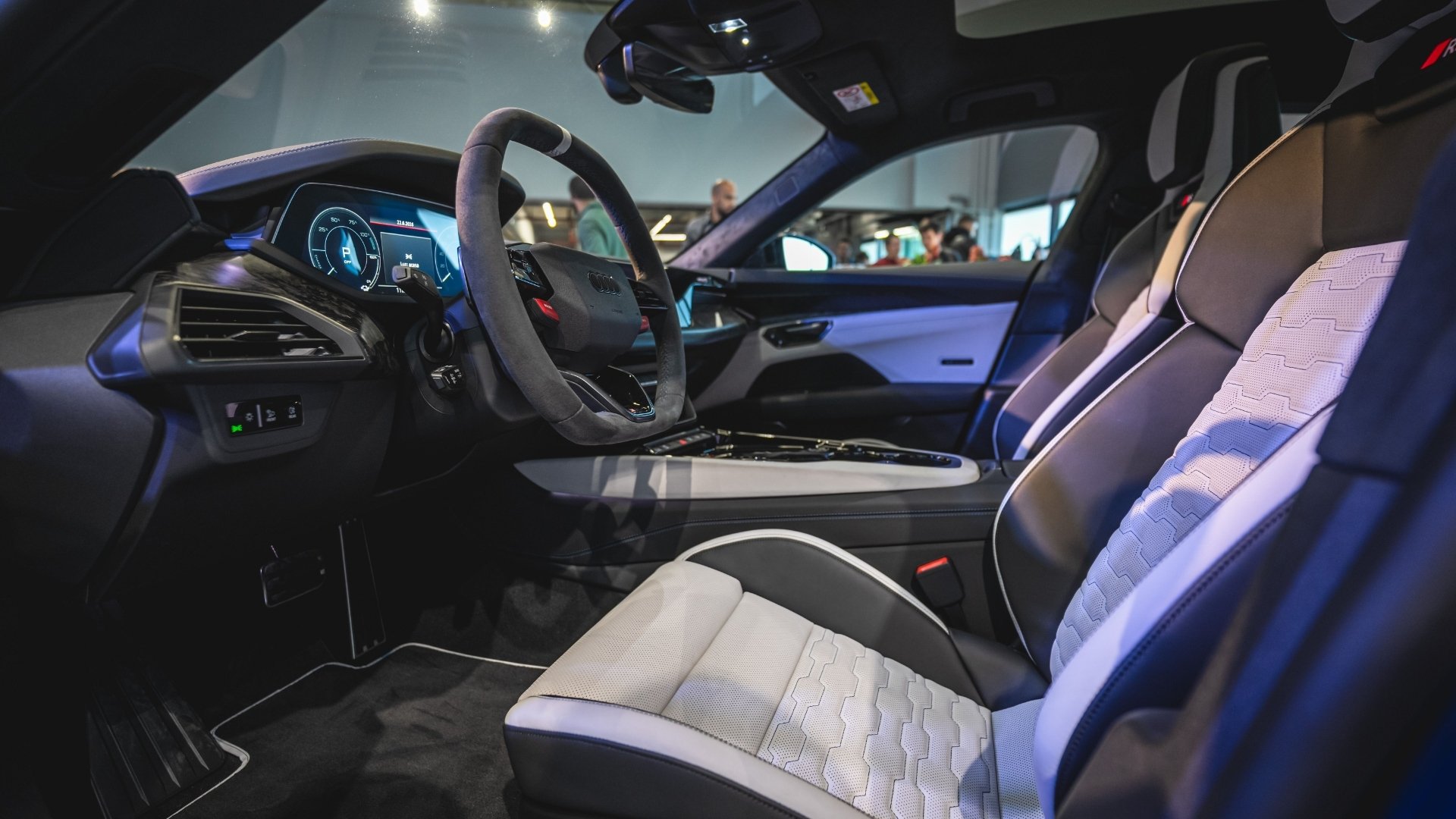 Interior view of a modern sports car, featuring a sleek dashboard, an advanced digital display, and stylish leather seats with gray and white accents.