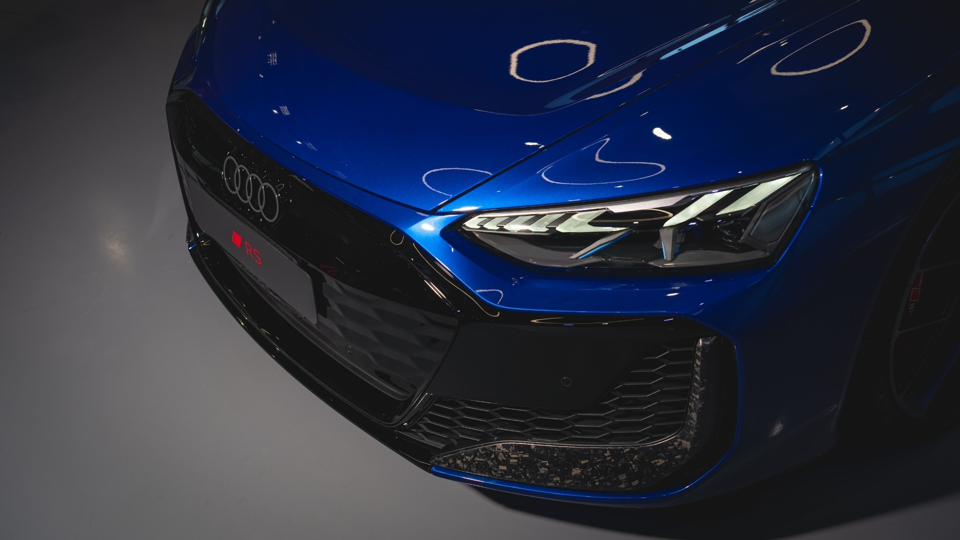 Close-up view of a blue Audi RS car's front end, showcasing the sleek headlights and sporty grille design.