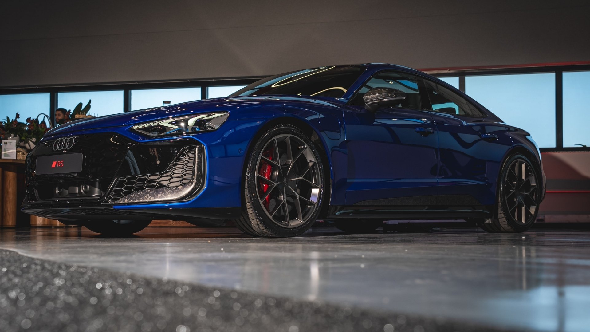A blue Audi RS sports car showcased in a well-lit indoor setting, featuring sleek design and modern wheels.