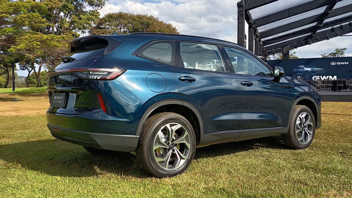 A side view of a blue SUV parked on grass, showcasing its sleek design and alloy wheels, with a backdrop of an outdoor event setup.