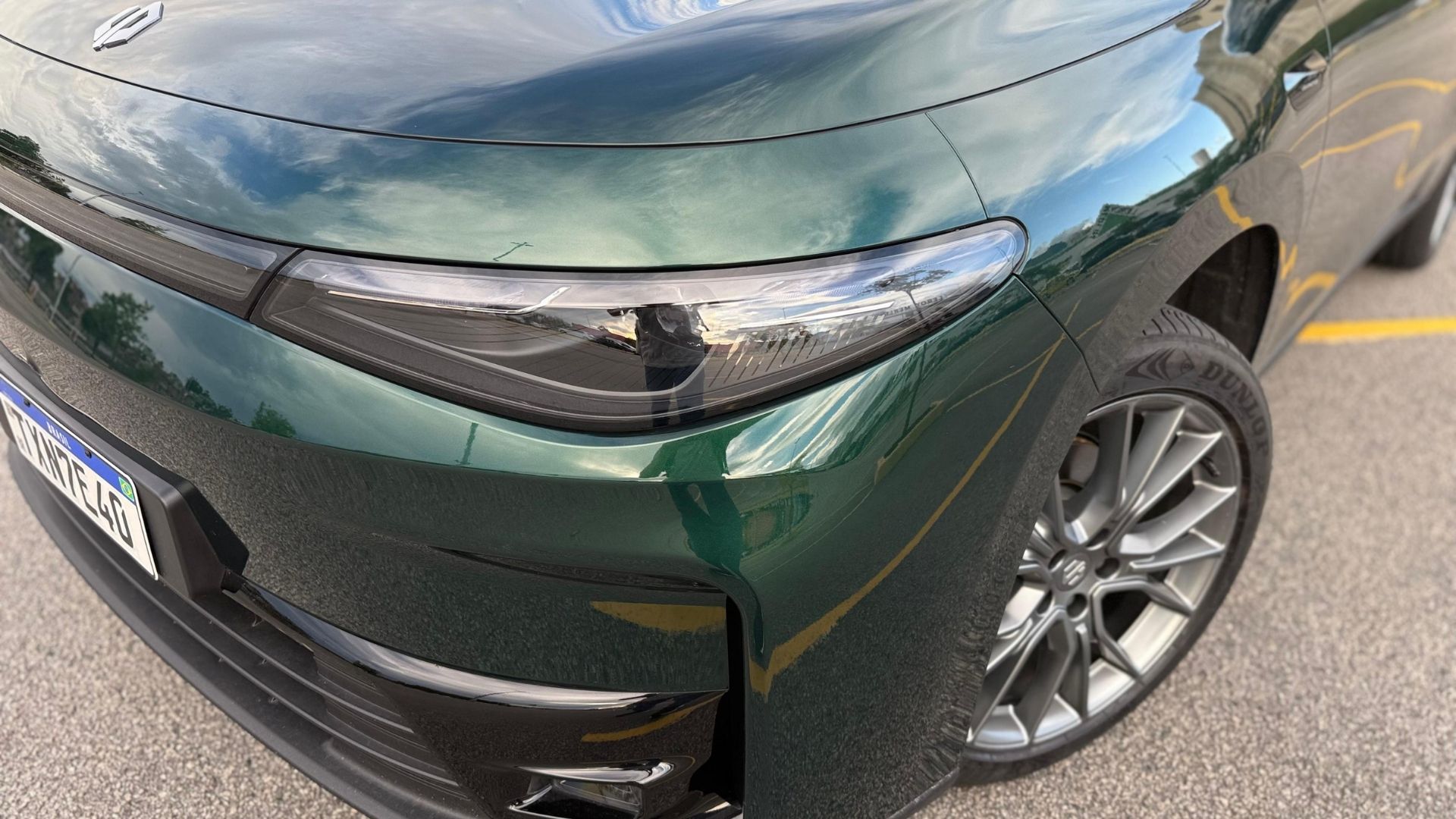 Close-up of the front corner of a green car, showcasing the sleek design, headlights, and stylish alloy wheel.