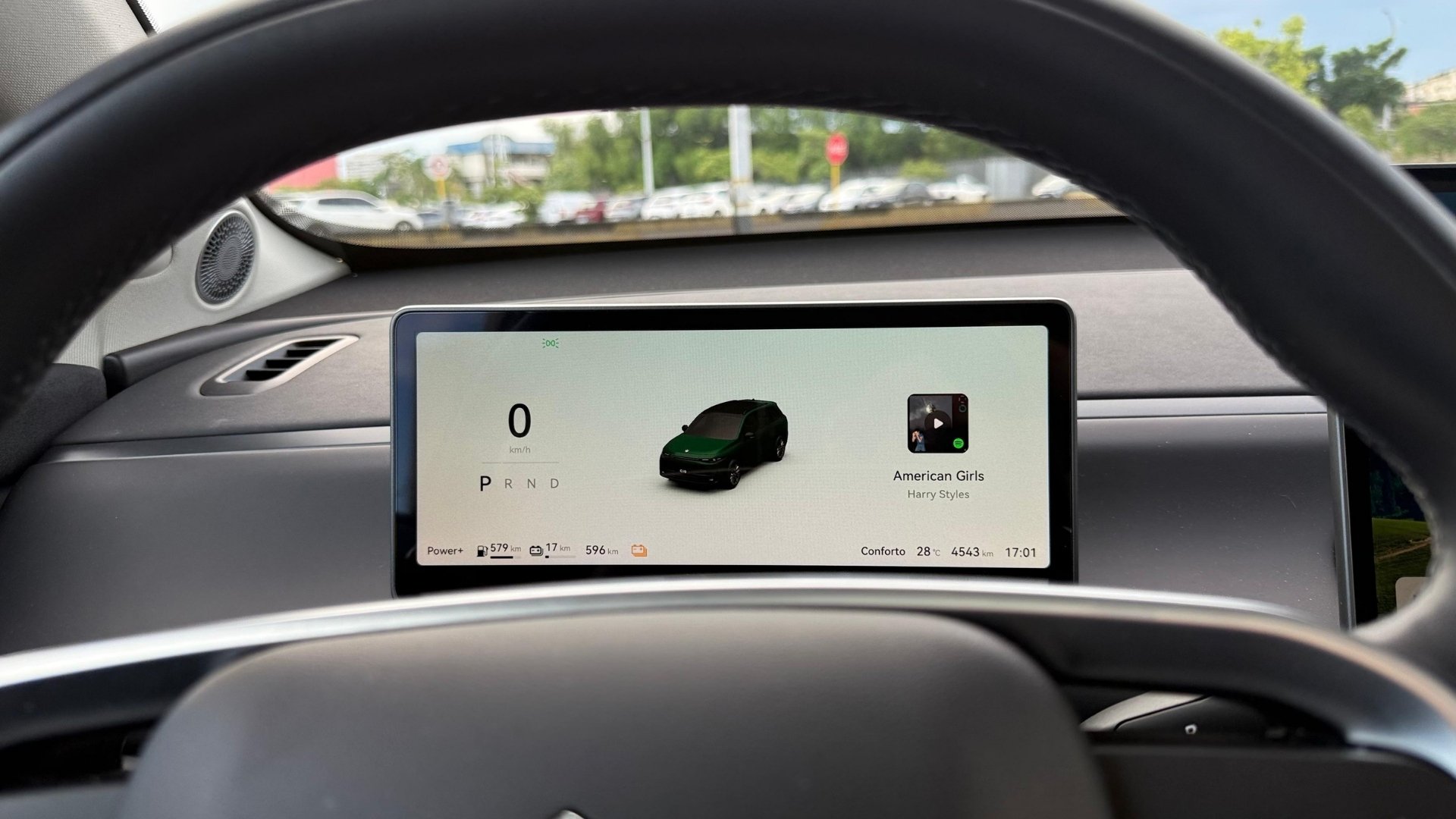 View of a car's dashboard displaying the speedometer at 0 km/h, gear indicators (P, R, N, D), battery range of 579 km, and currently playing music 'American Girls' by Harry Styles.