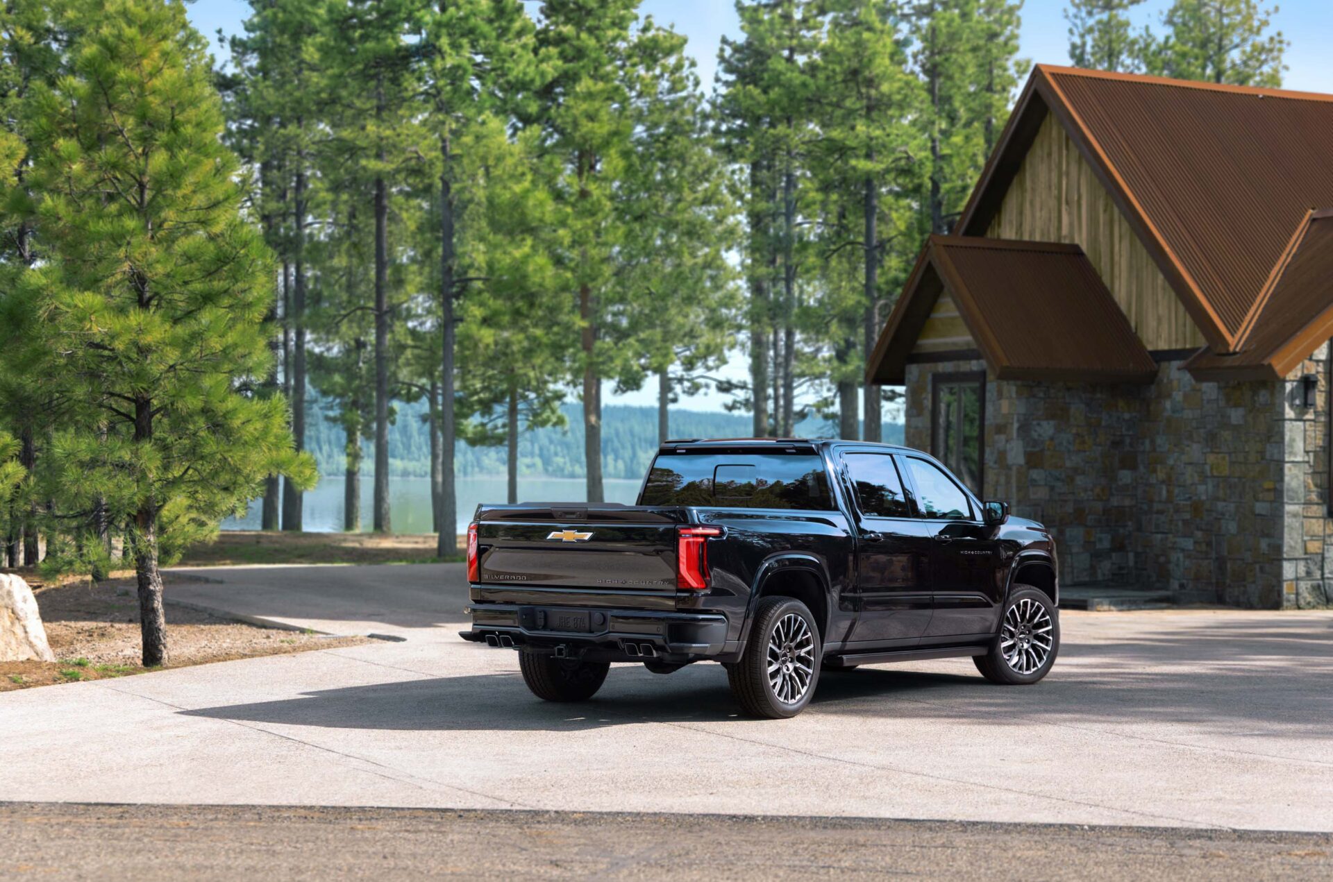 A black Chevrolet Silverado parked on a driveway near a house, with tall trees and a lake visible in the background.