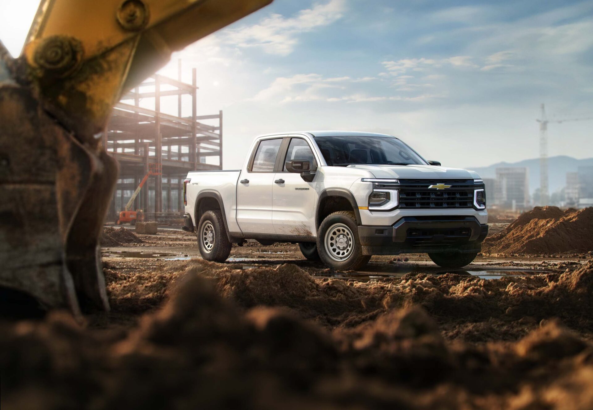 A white pickup truck parked on a construction site, with dirt and construction materials in the foreground and steel framework in the background.