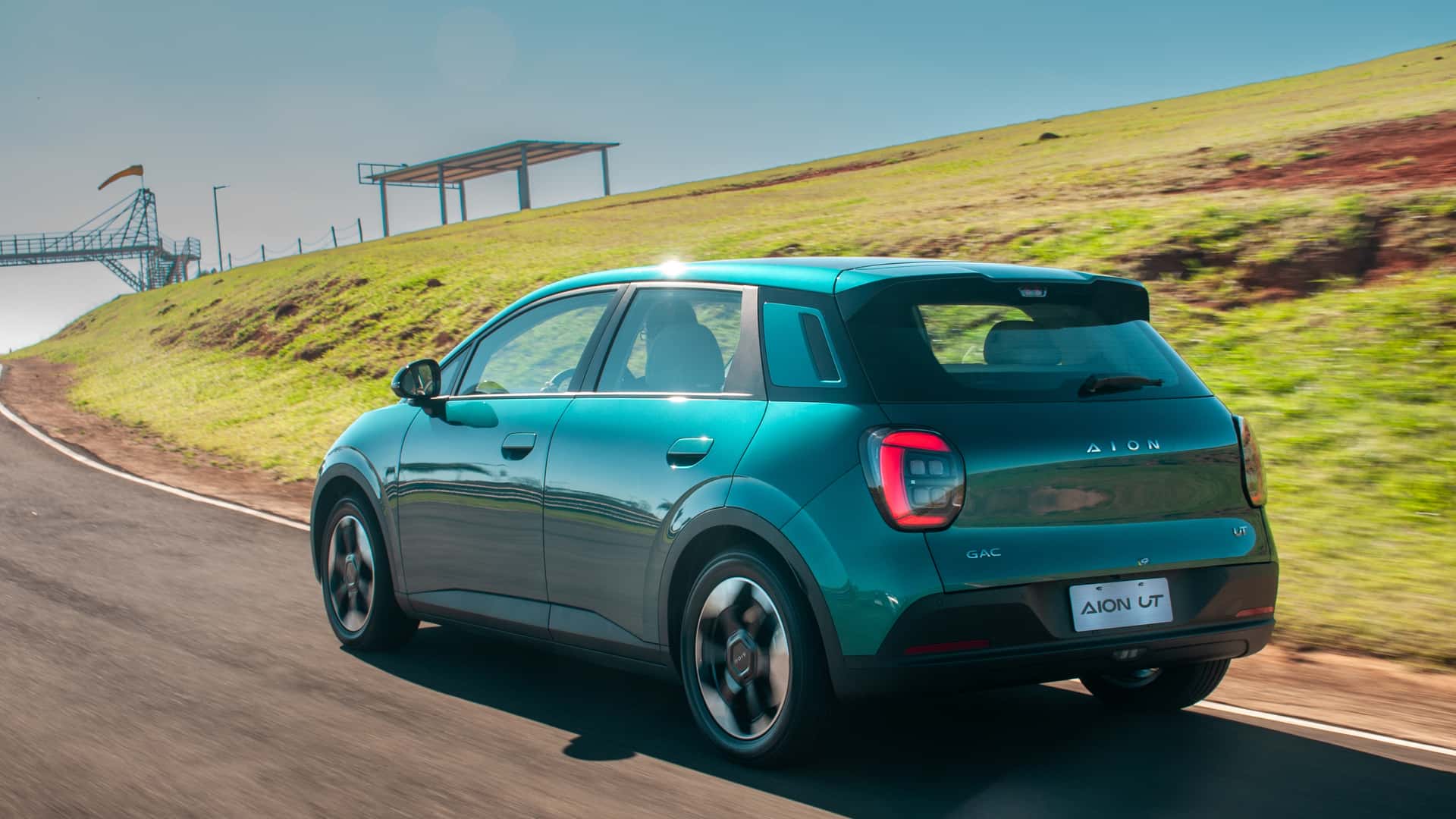 A teal electric car driving on a winding road with green hills in the background.