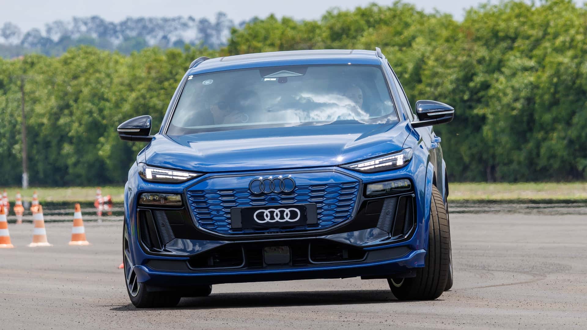 A blue Audi SUV driving on a track with cones in the background and greenery in the distance.