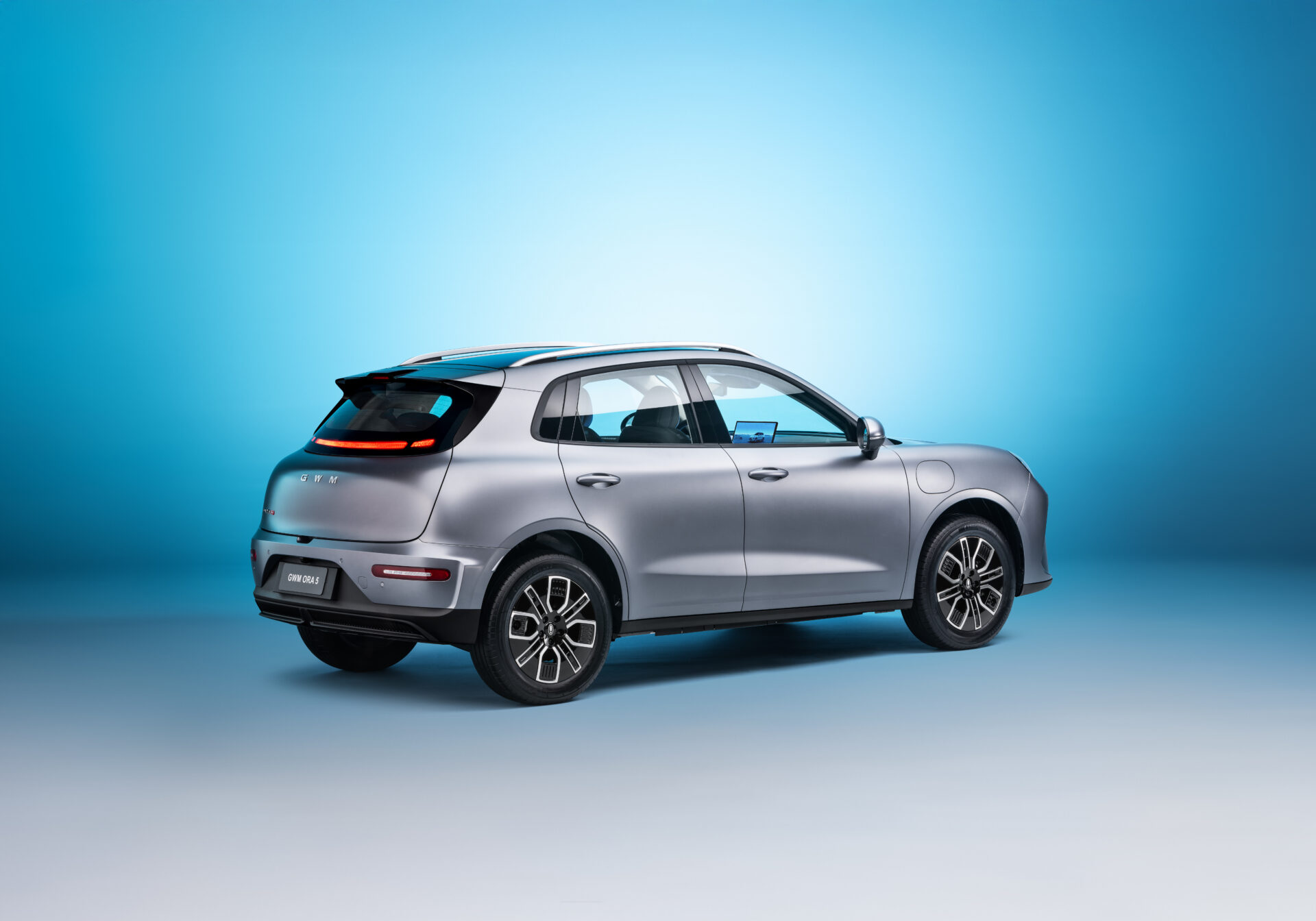 A sleek silver electric vehicle with a modern design, shown from the rear on a gradient blue background.