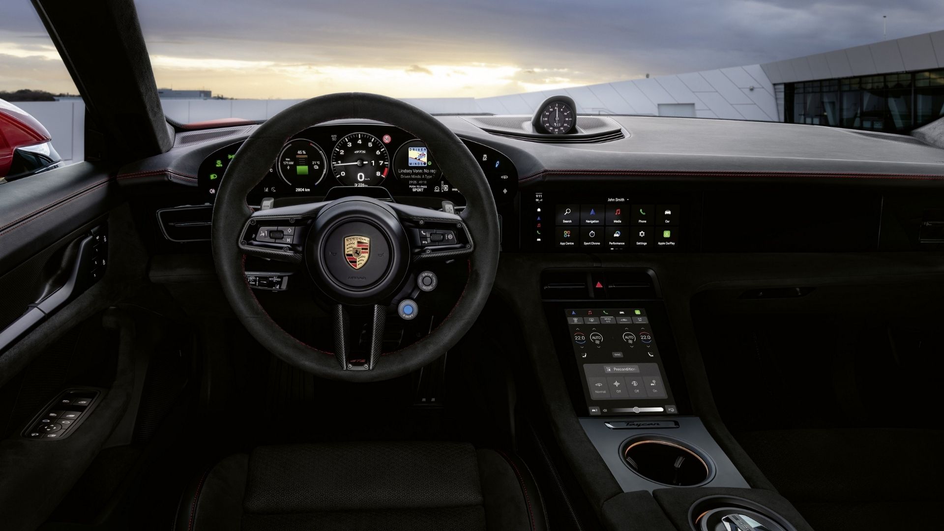 Interior view of a modern Porsche sports car showcasing the steering wheel with a logo, digital displays, and sleek dashboard design against a scenic background.