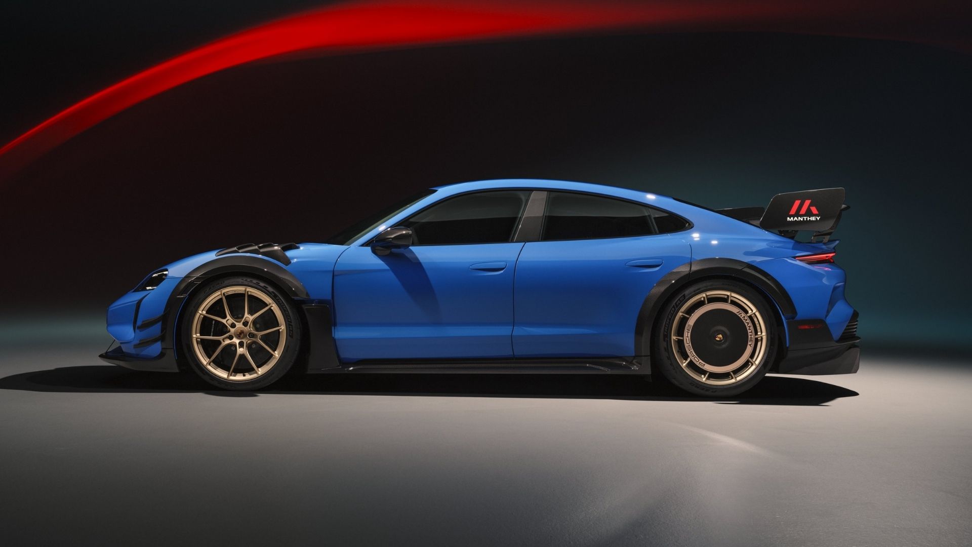 A blue sports car featuring a sleek design, bold aerodynamic enhancements, and distinctive gold rims, displayed in a dramatic lighting setting.