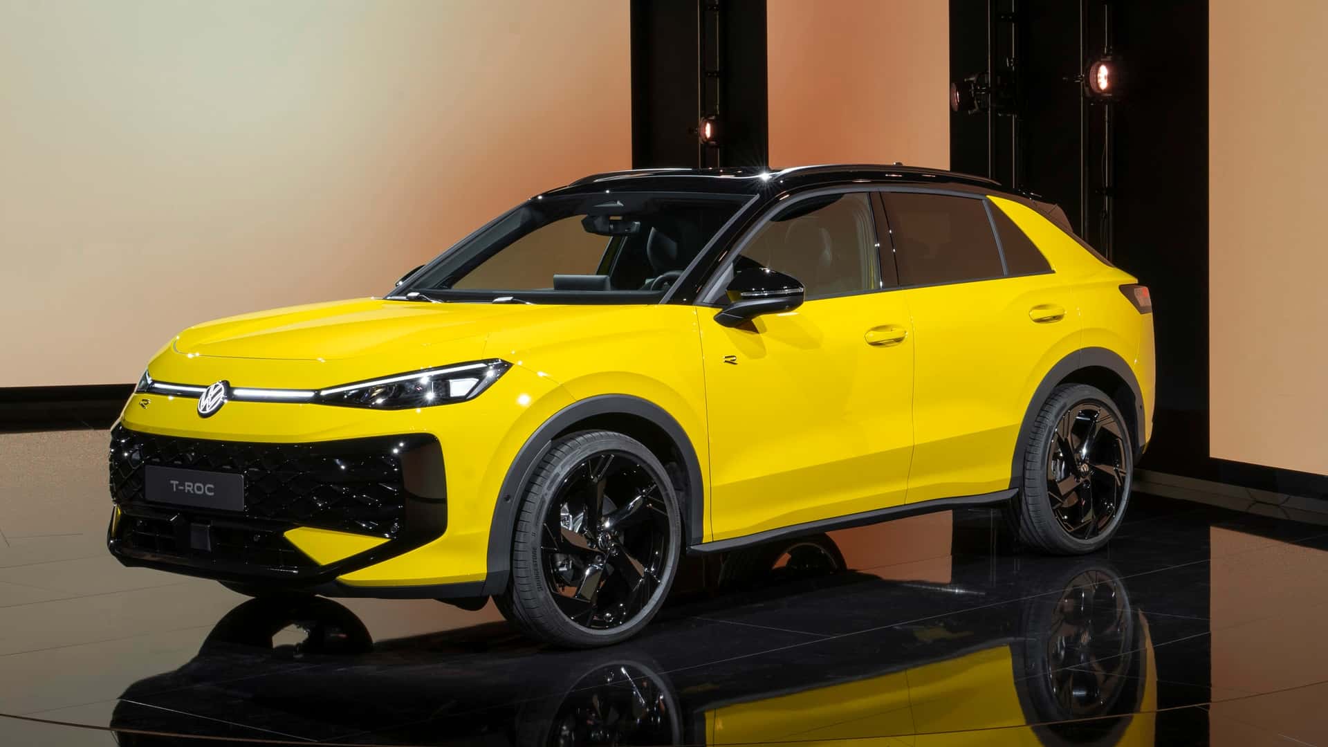A vibrant yellow Volkswagen T-Roc displayed in a modern studio setting, showcasing its sleek design and black accents.