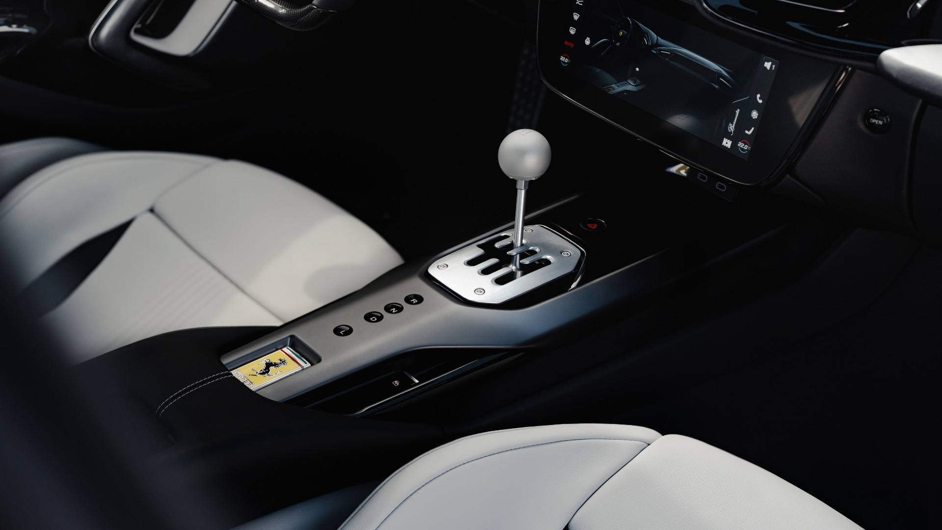 Close-up of a car's center console featuring a manual gear shifter and control buttons, with black and white leather seats visible.
