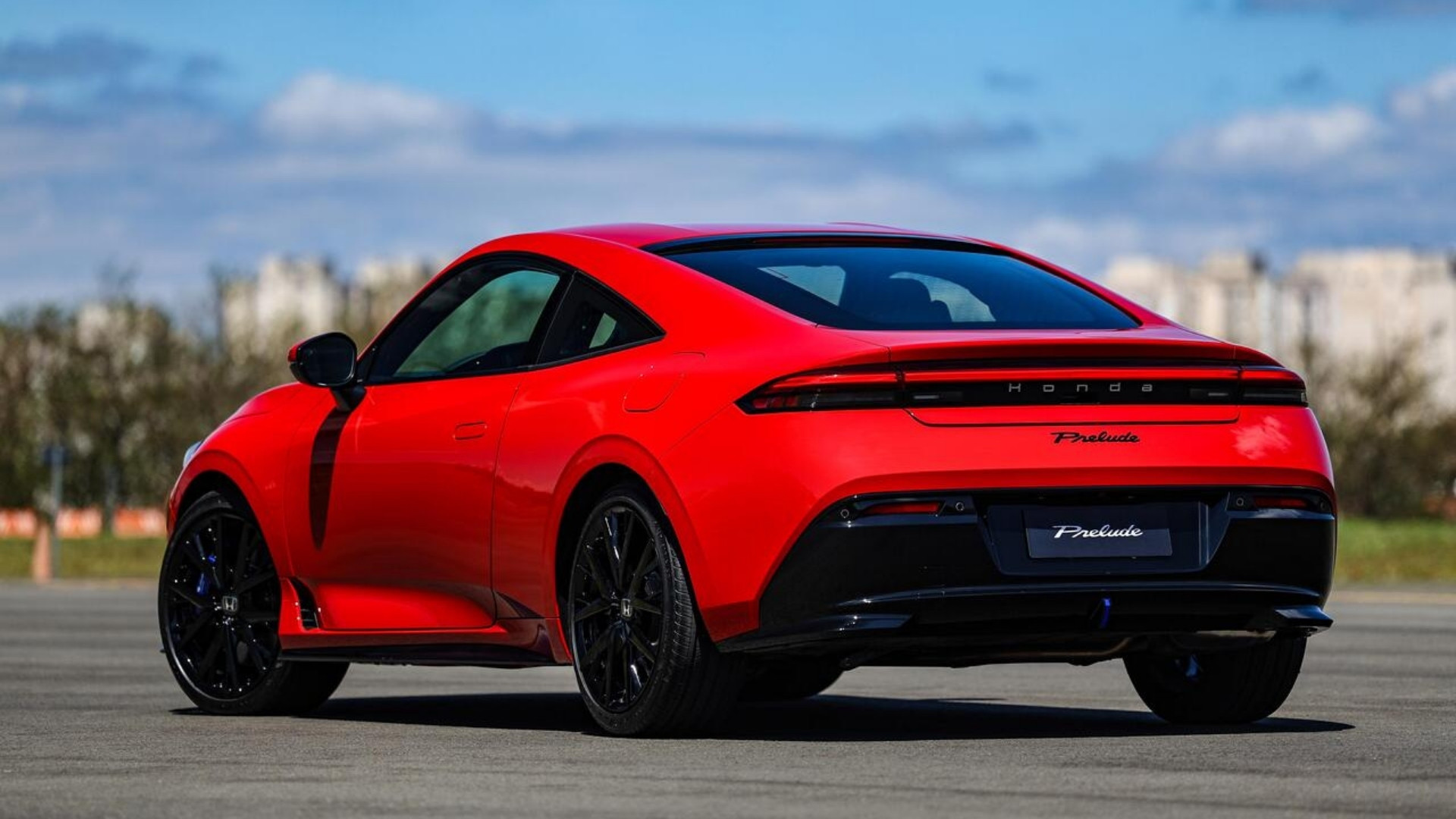 A red Honda Prelude sports car viewed from the rear, showcasing its sleek design and black alloy wheels against a blue sky.