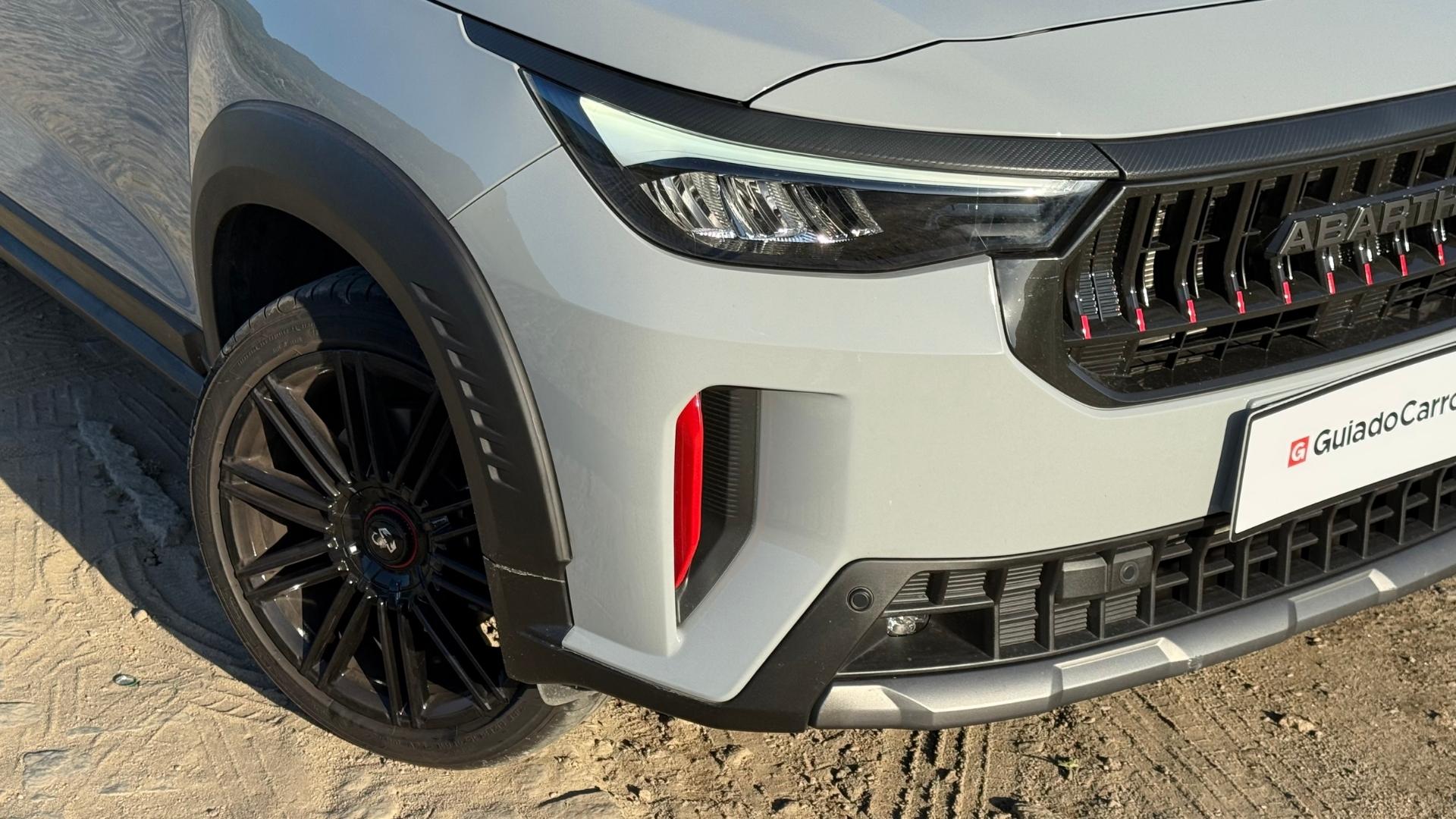 Close-up of a stylish car front featuring a sleek grille with the 'Abarth' logo, modern headlights, black wheel with a unique design, and a sporty bumper.
